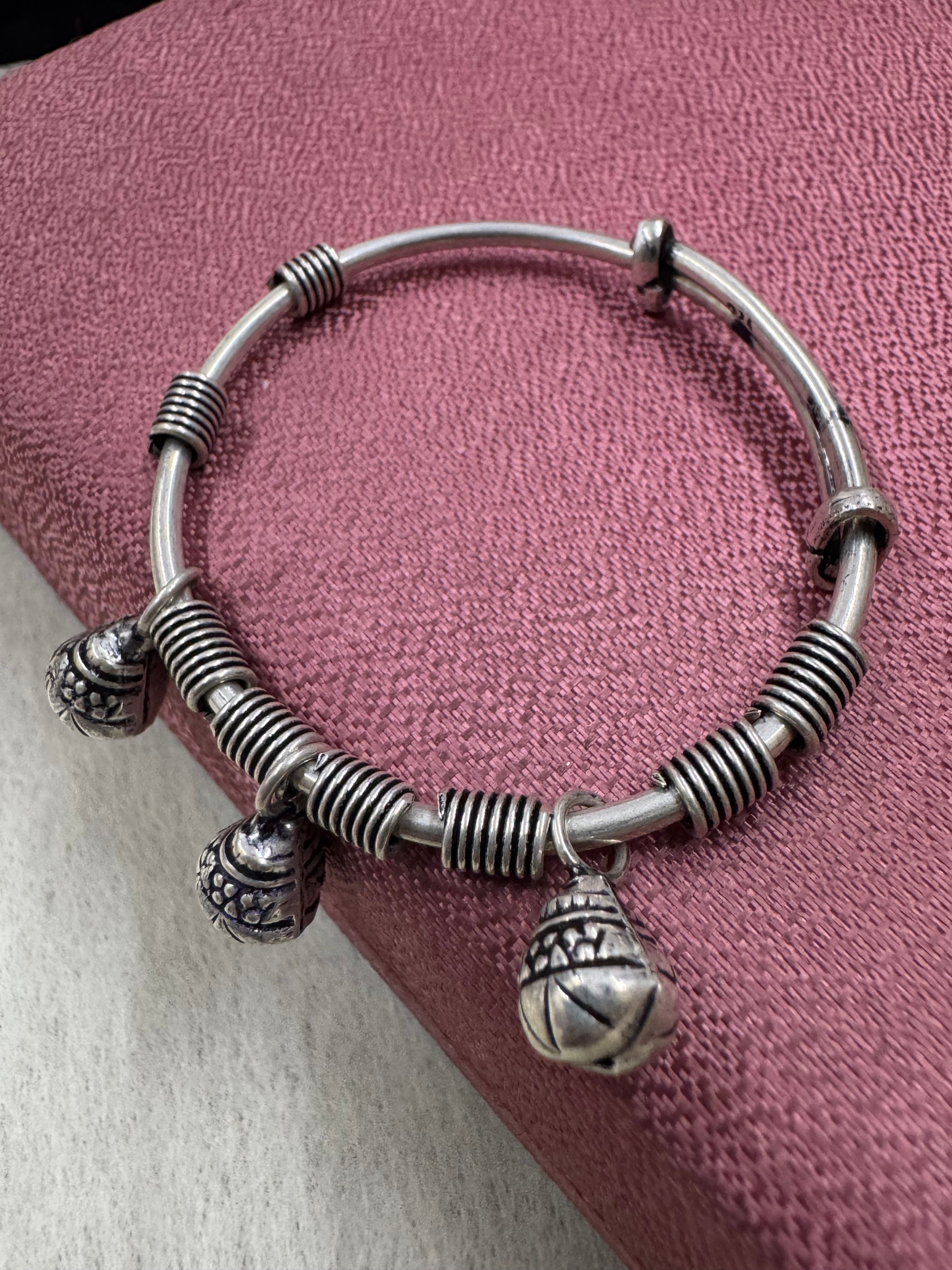 Sterling silver adjustable bangle with coiled wire blocks and three ghungroo bells, resting on dusty pink fabric.
