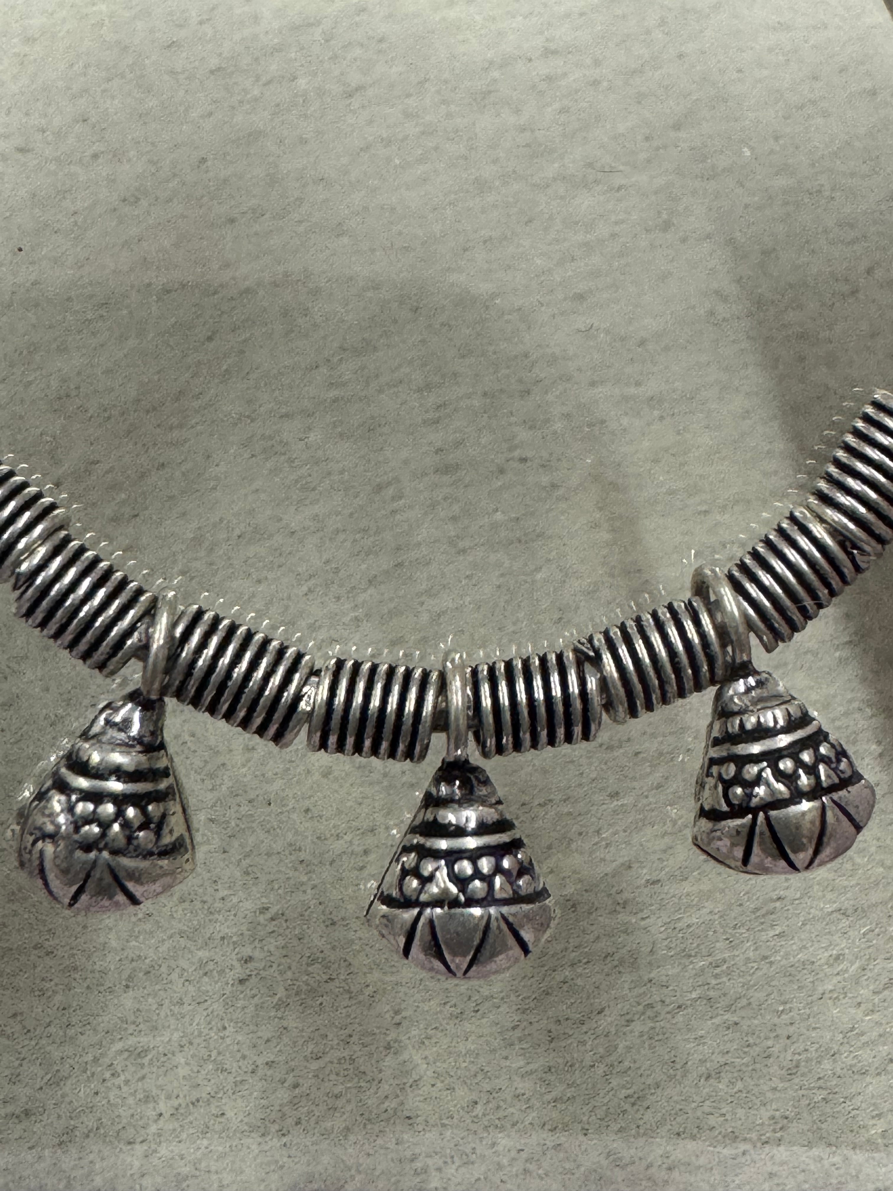 Close view of the oxidised coiled wire and three ghungroo bells hanging from the sterling silver bangle.