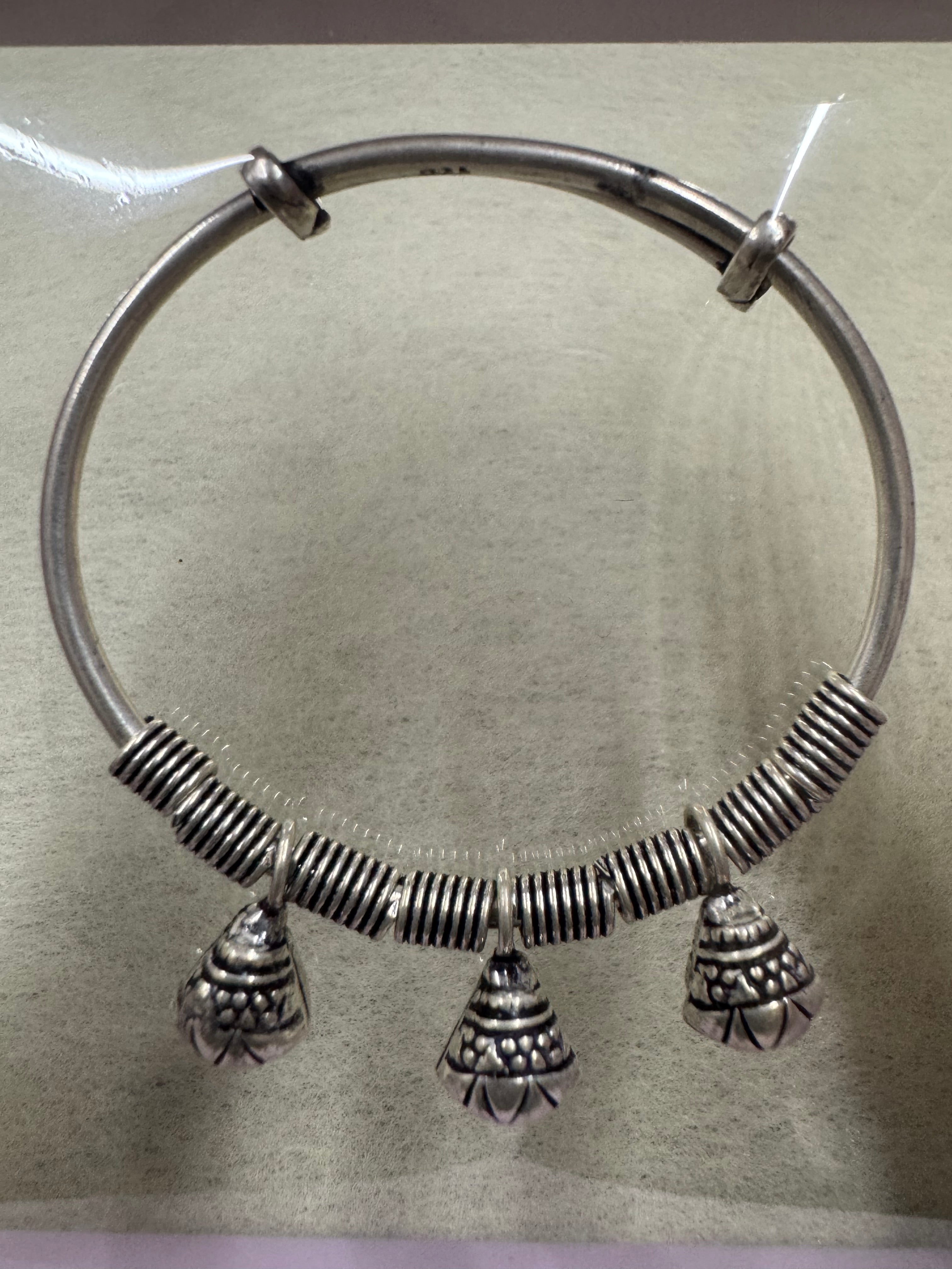 Sterling silver bangle laid flat on paper, showing the coiled front half and the plain sliding ends.