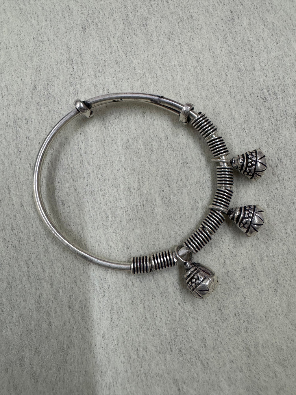 Sterling silver adjustable bangle on a pale ground, showing the bell slits and the 925 stamp on the plain band.