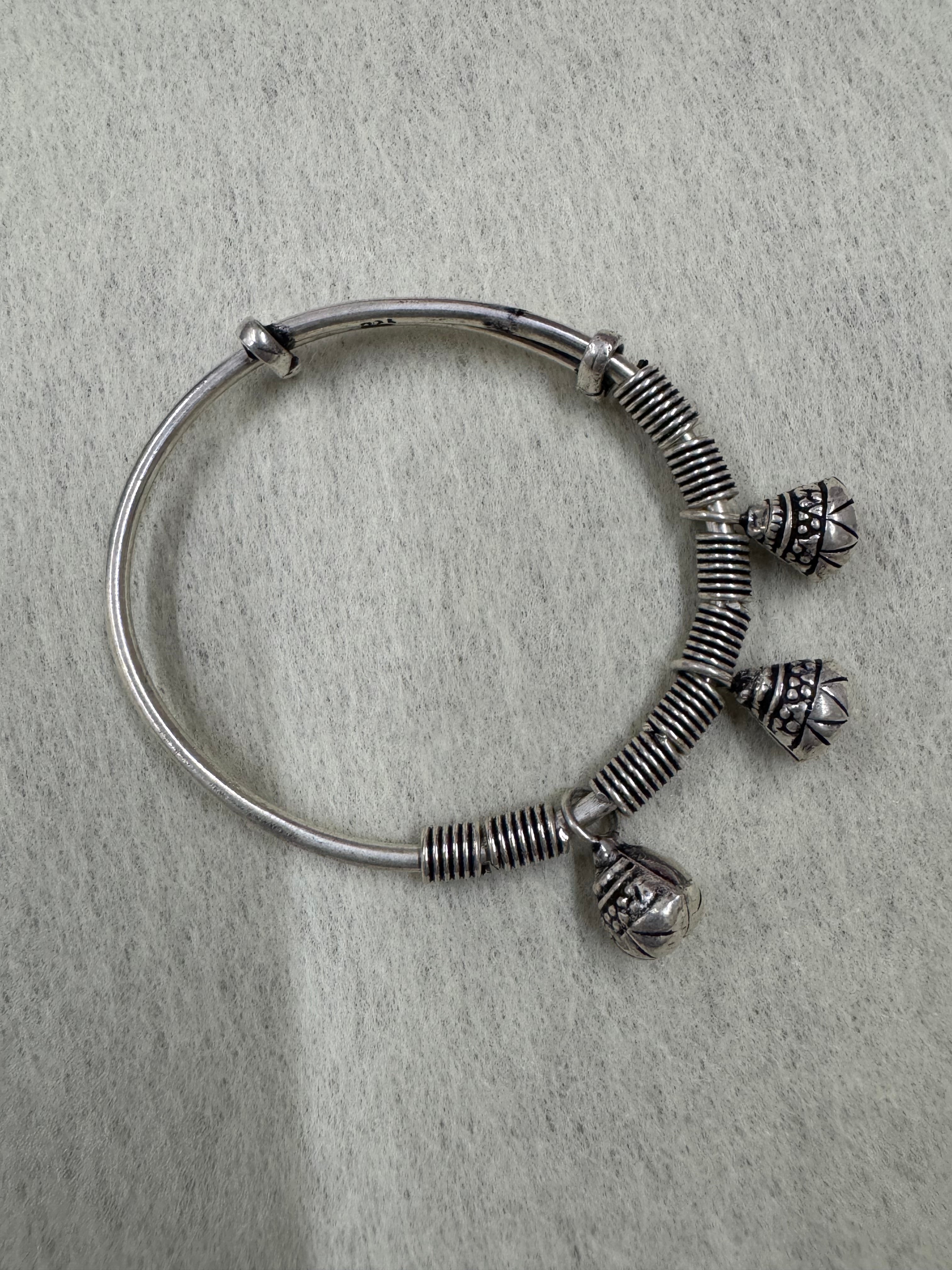 Sterling silver adjustable bangle on a pale ground, showing the bell slits and the 925 stamp on the plain band.