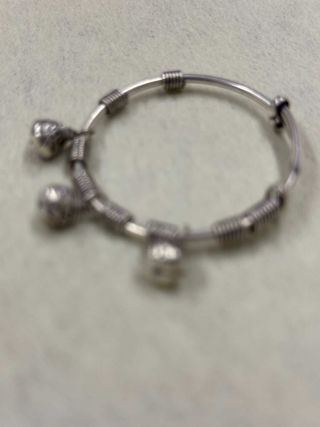 Soft-focus overhead view of the sterling silver bangle showing the coiled sections and the three bells.