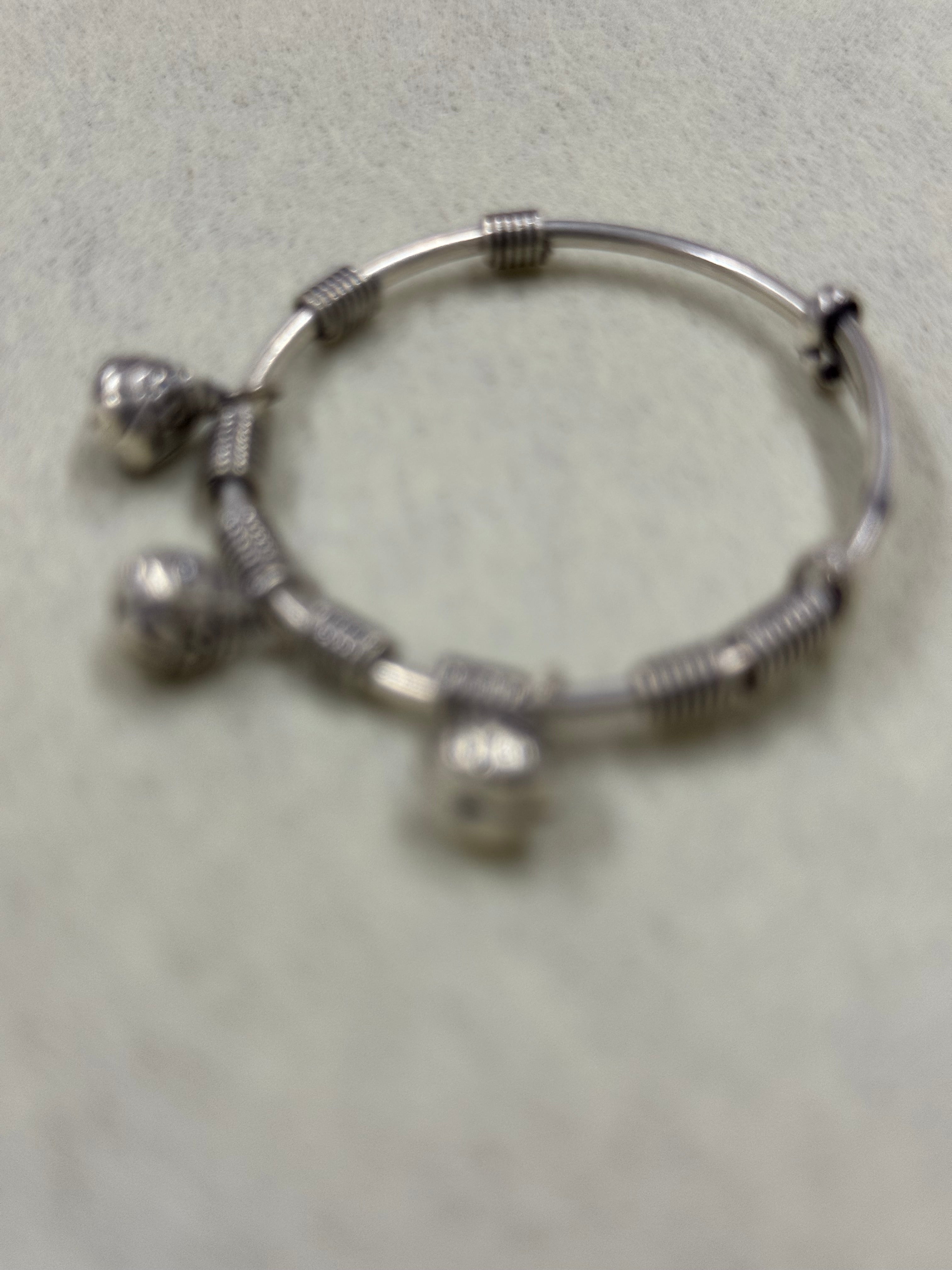 Soft-focus overhead view of the sterling silver bangle showing the coiled sections and the three bells.