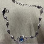 Sterling silver evil eye bracelet laid in a curve, showing the leaf-engraved marquise links, extender chain and clasp.