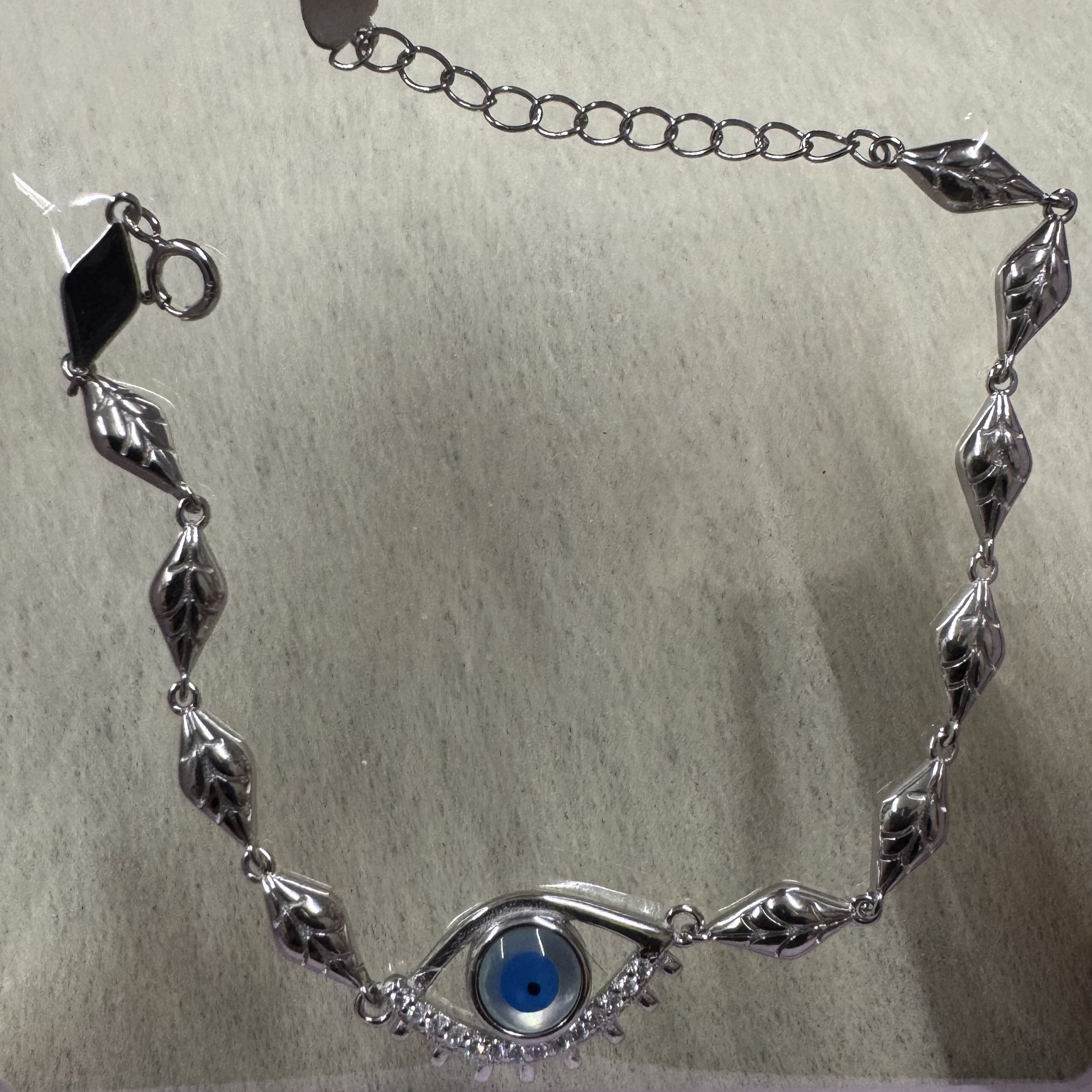 Sterling silver evil eye bracelet laid in a curve, showing the leaf-engraved marquise links, extender chain and clasp.