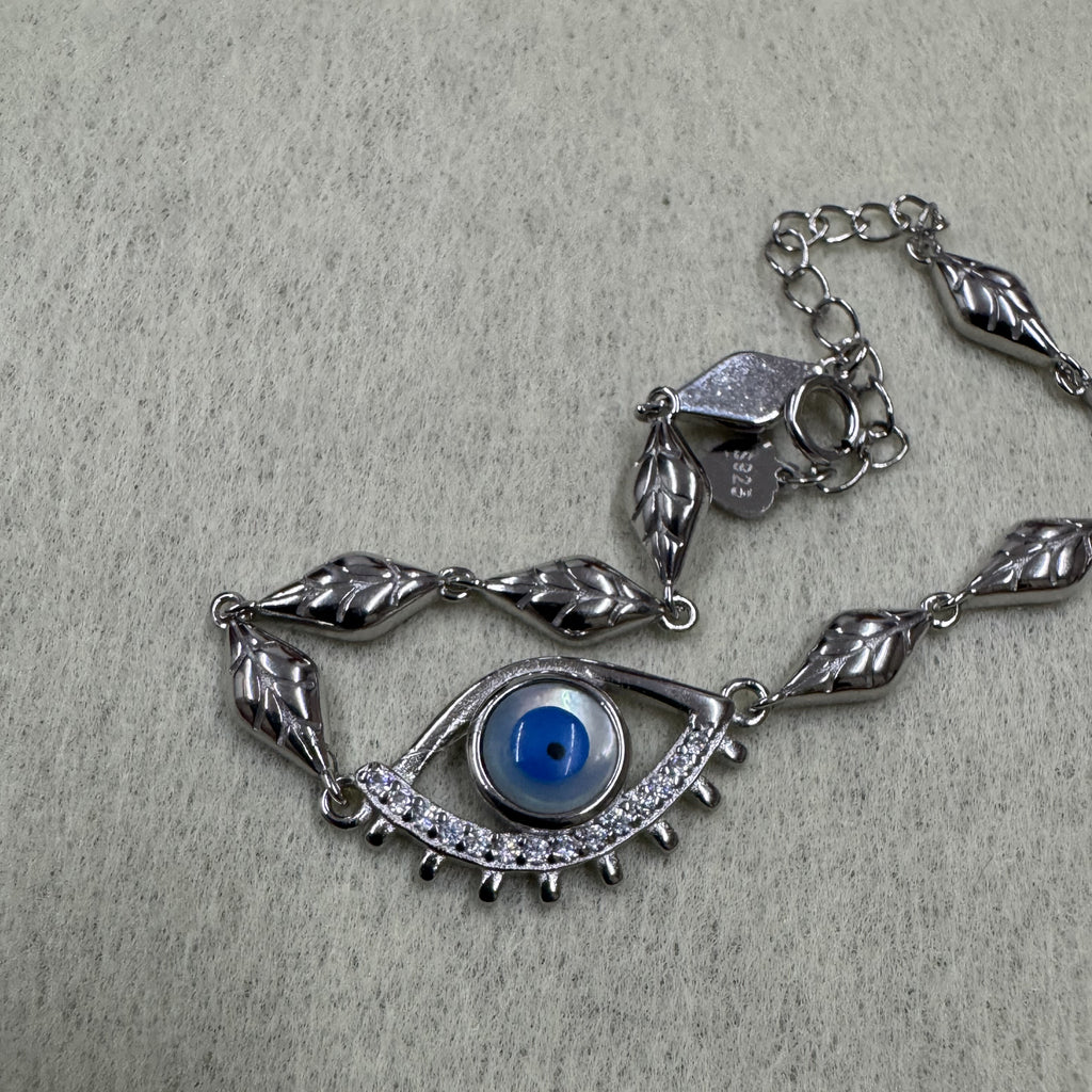 Angled view of the sterling silver nazar eye bracelet with its cubic zirconia lower lid, spring ring clasp and stamped tag.