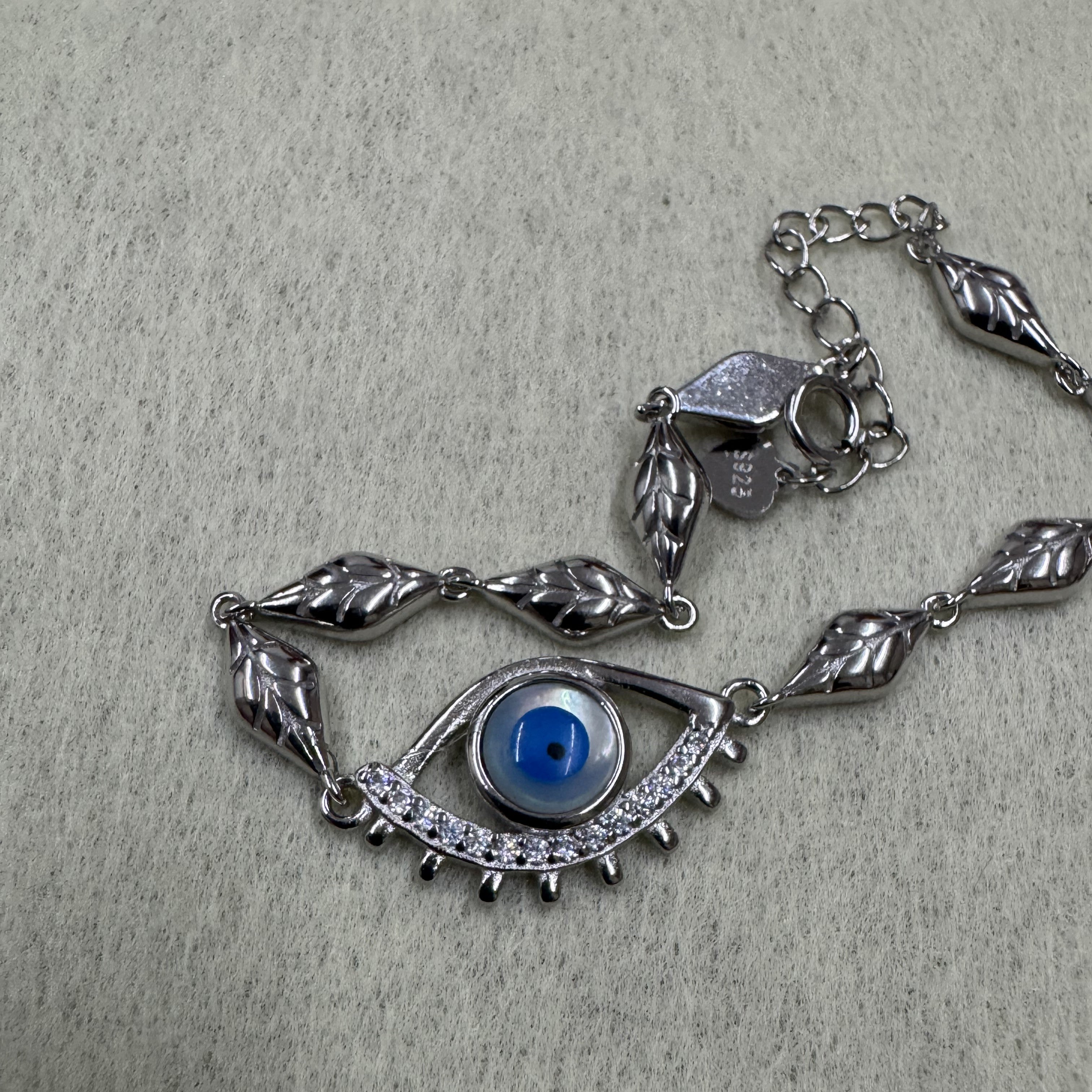 Angled view of the sterling silver nazar eye bracelet with its cubic zirconia lower lid, spring ring clasp and stamped tag.