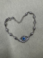 Sterling silver evil eye bracelet arranged on a pale grey ground, the eye at one end and the extender chain at the other.