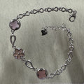 Sterling silver bracelet with two pink quatrefoil discs, a pink flower set with cubic zirconia, and a bow-link chain with lobster clasp.
