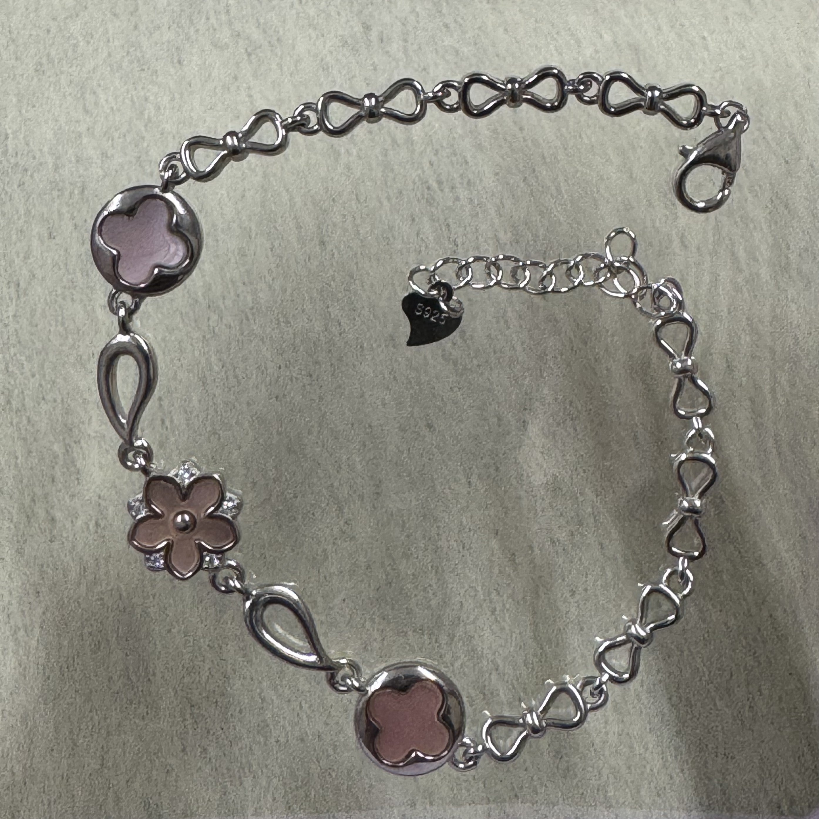 Sterling silver bracelet with two pink quatrefoil discs, a pink flower set with cubic zirconia, and a bow-link chain with lobster clasp.