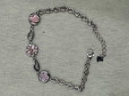 Sterling silver station bracelet laid open on a pale ground, showing the pear-shaped links between the pink stations.