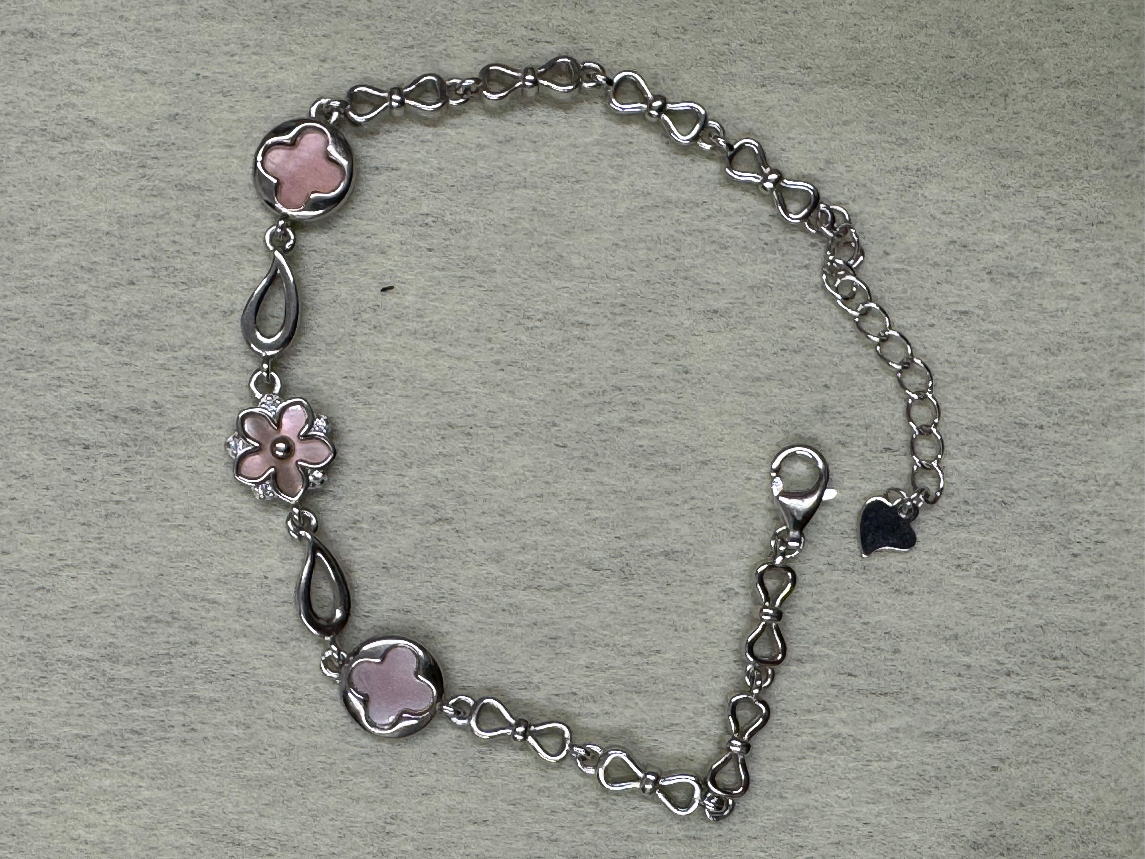 Sterling silver station bracelet laid open on a pale ground, showing the pear-shaped links between the pink stations.