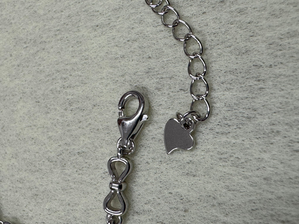 Close view of the lobster clasp, extender chain and stamped heart tag on the sterling silver bracelet.
