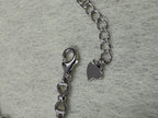 Close view of the lobster clasp, extender chain and stamped heart tag on the sterling silver bracelet.
