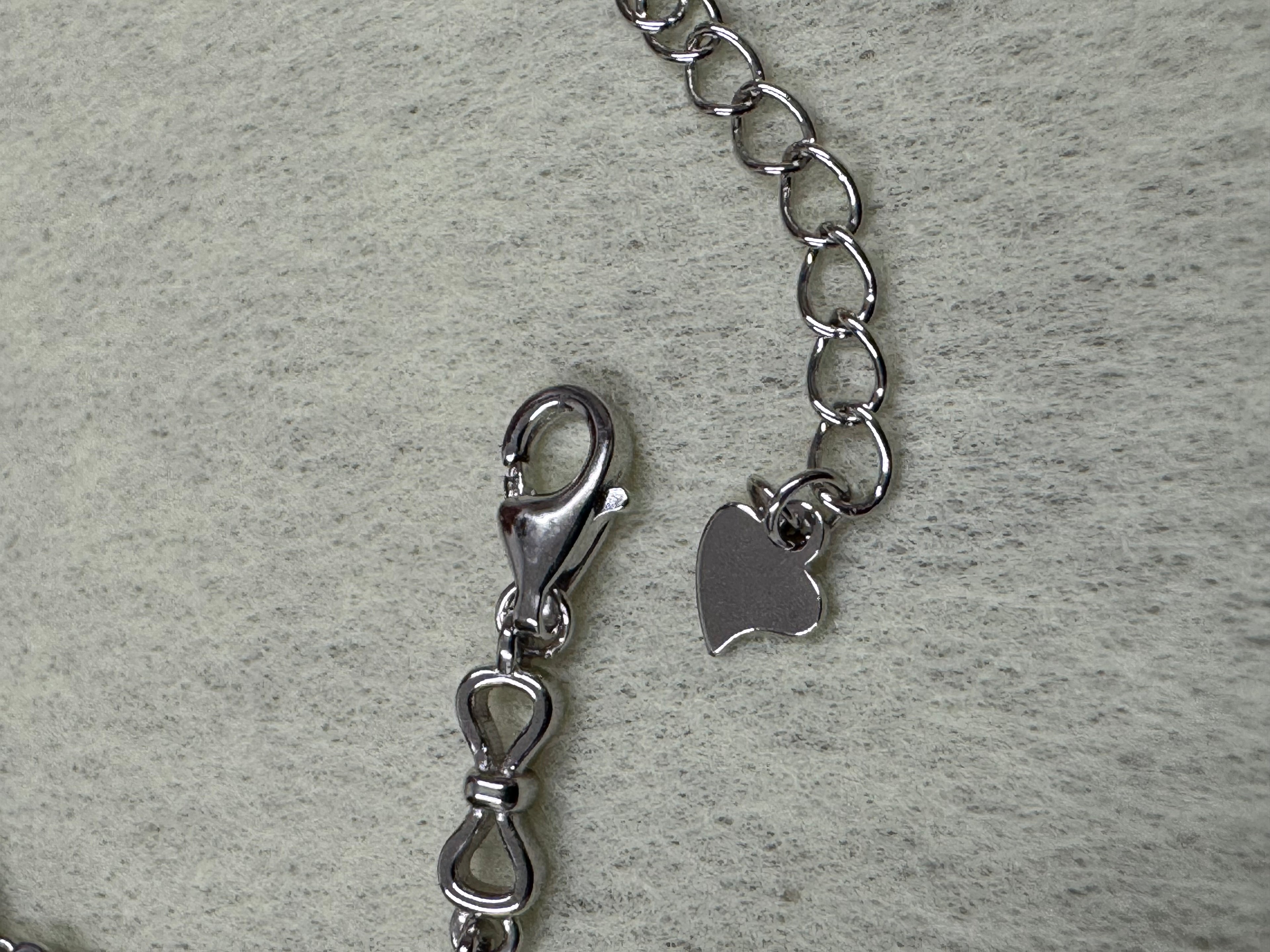 Close view of the lobster clasp, extender chain and stamped heart tag on the sterling silver bracelet.