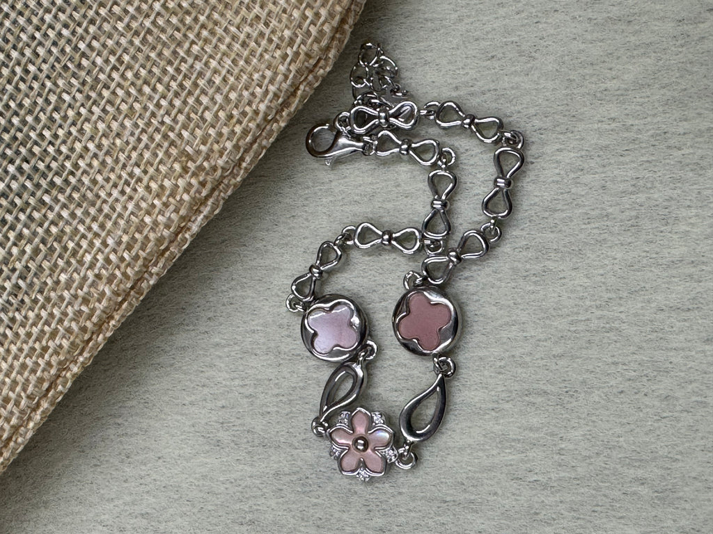 Sterling silver bracelet with its pink flower and quatrefoil stations, coiled beside woven jute cloth.