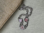 Sterling silver bracelet with its pink flower and quatrefoil stations, coiled beside woven jute cloth.
