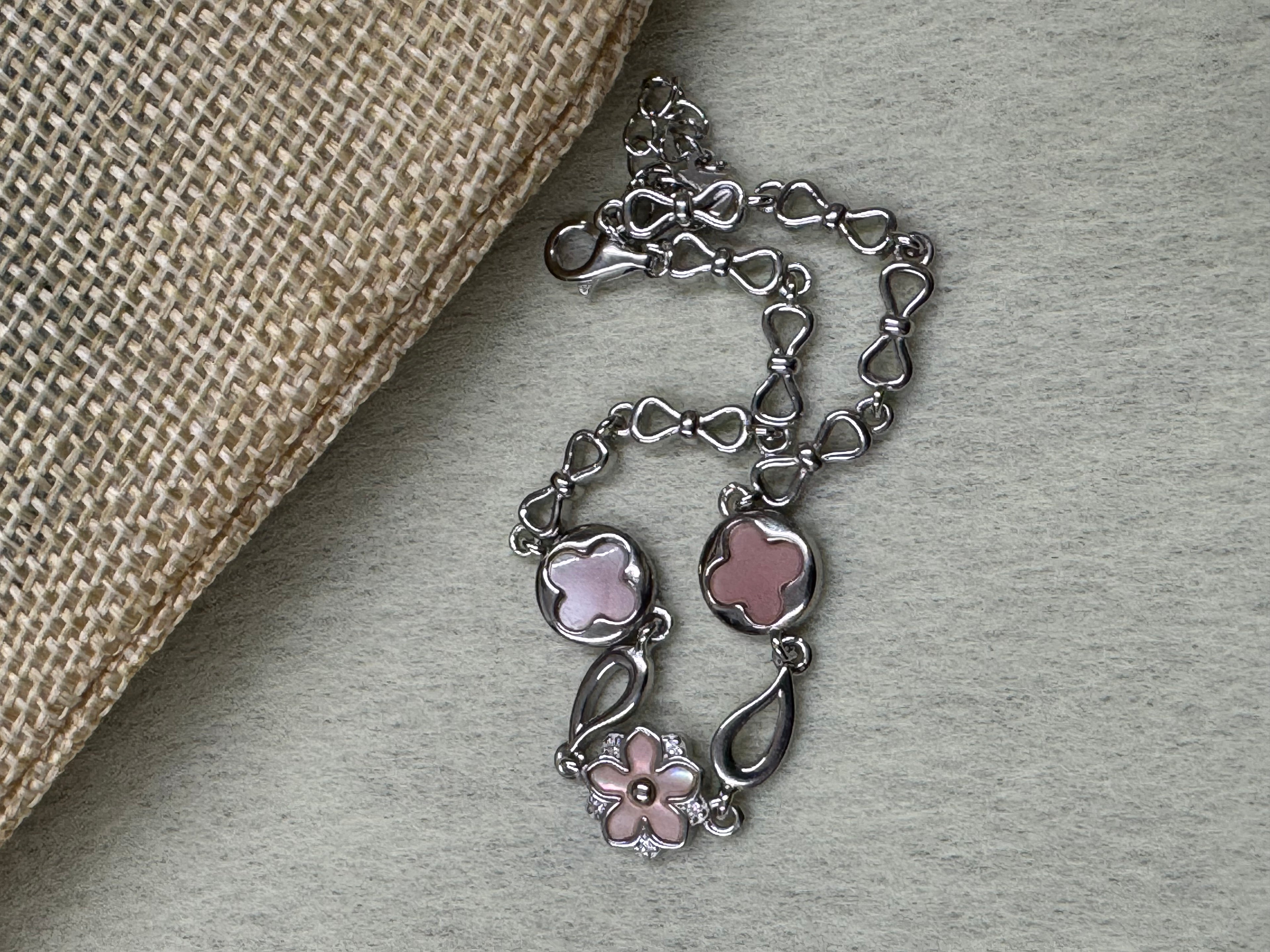 Sterling silver bracelet with its pink flower and quatrefoil stations, coiled beside woven jute cloth.