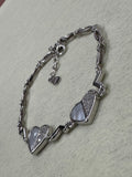 Sterling silver bracelet with two heart stations set with cubic zirconia, laid on woven beige fabric.