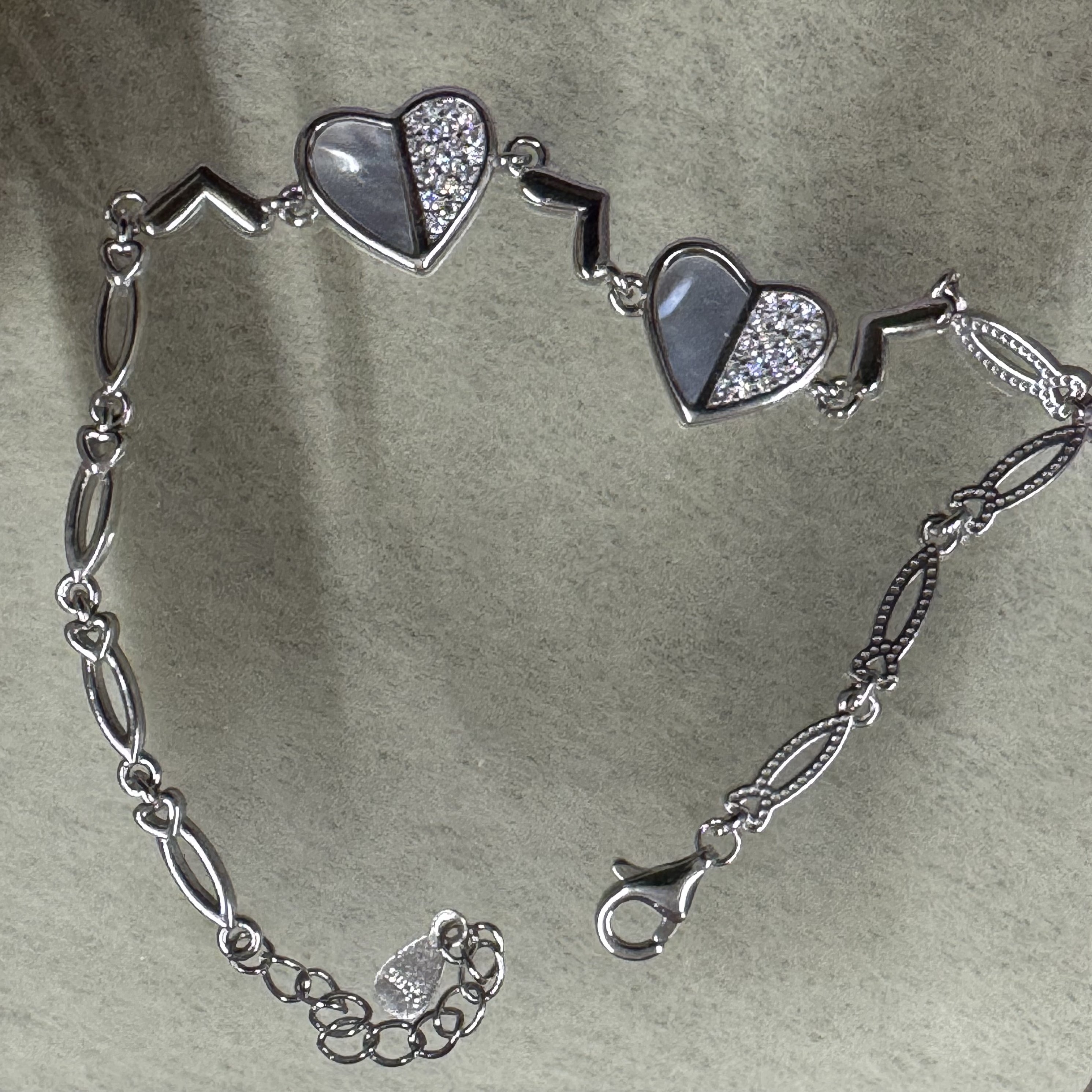 The sterling silver heart bracelet opened out on grey felt, showing the lobster clasp, extender chain and navette links.