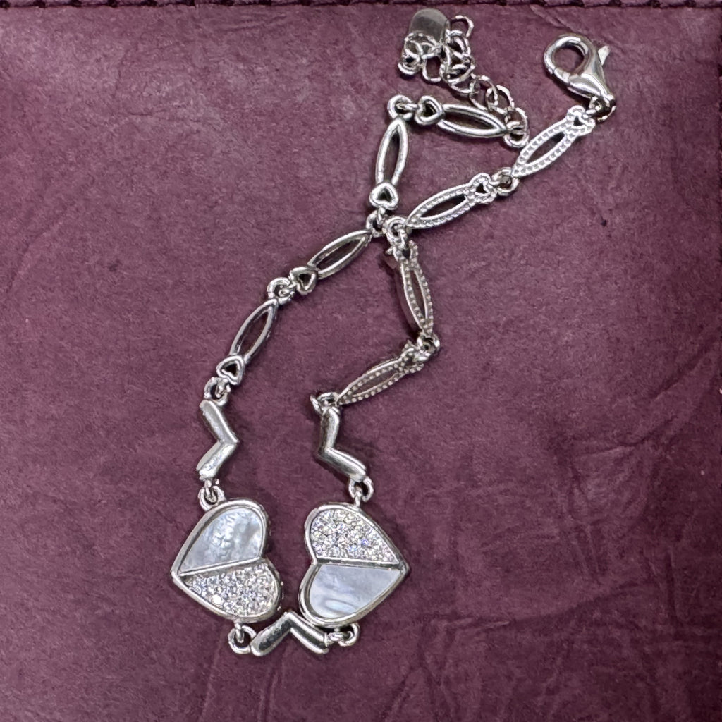 The sterling silver cubic zirconia heart bracelet arranged on a deep plum leather surface.