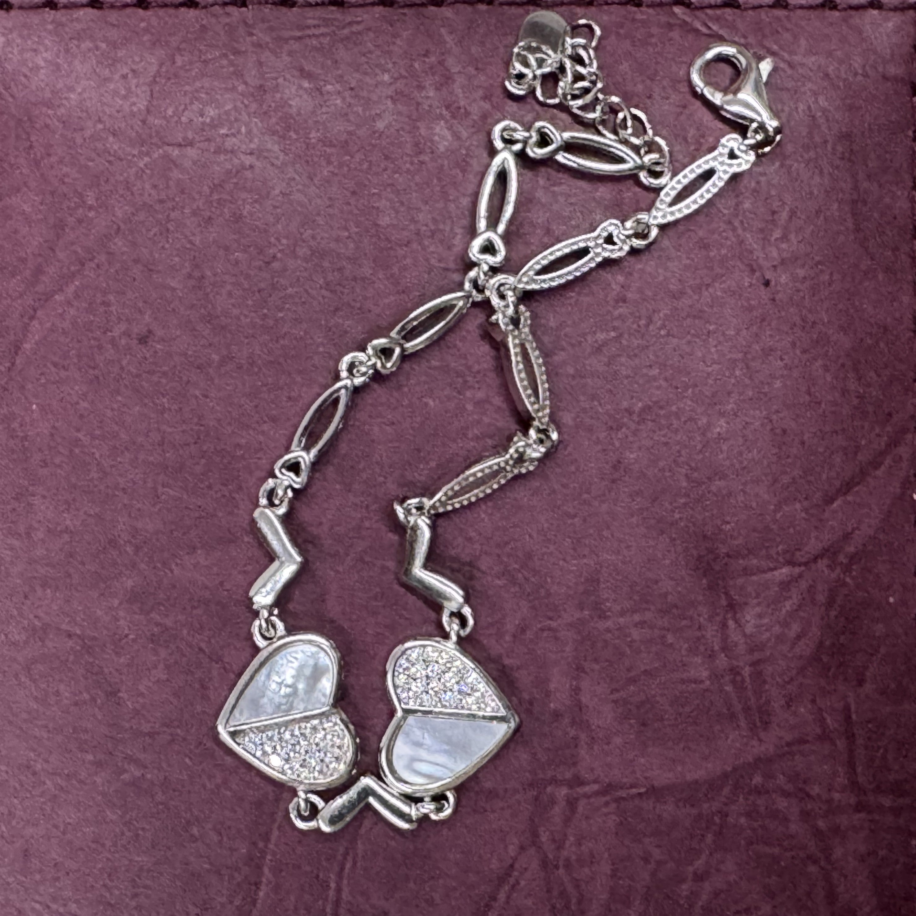 The sterling silver cubic zirconia heart bracelet arranged on a deep plum leather surface.