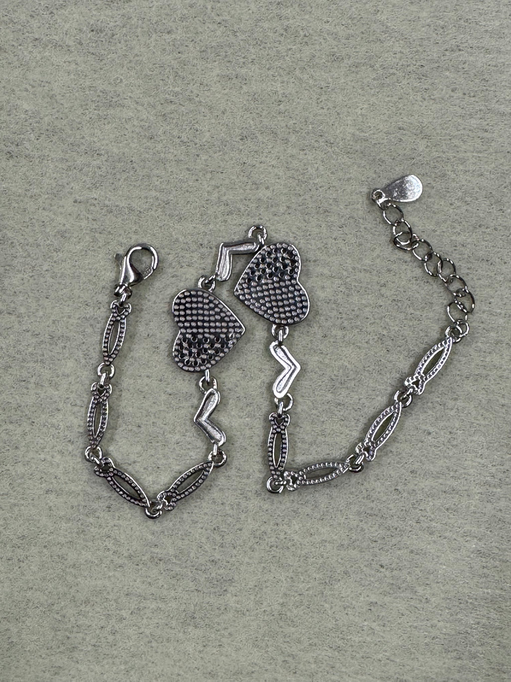 The sterling silver heart bracelet seen from the reverse on grey felt, with the lobster clasp and extender chain at the upper edge.