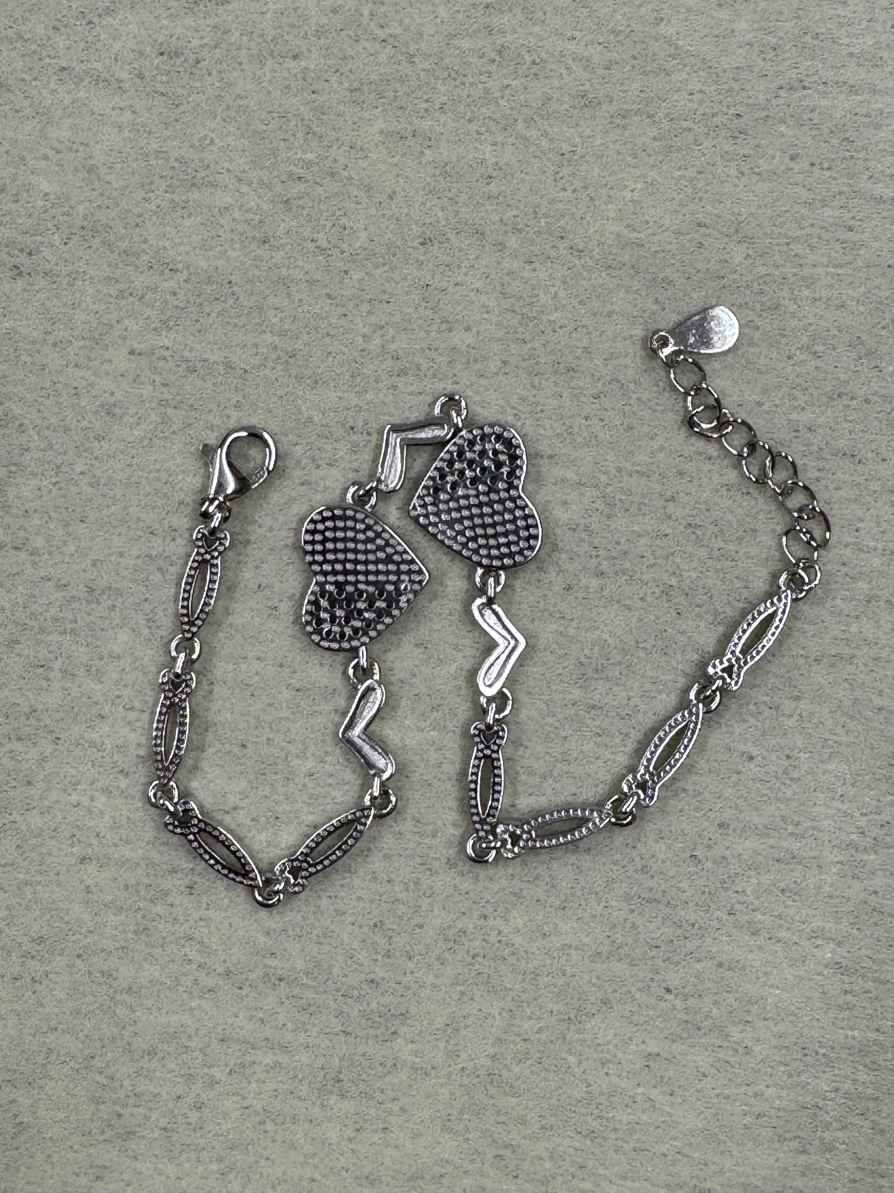 The sterling silver heart bracelet seen from the reverse on grey felt, with the lobster clasp and extender chain at the upper edge.