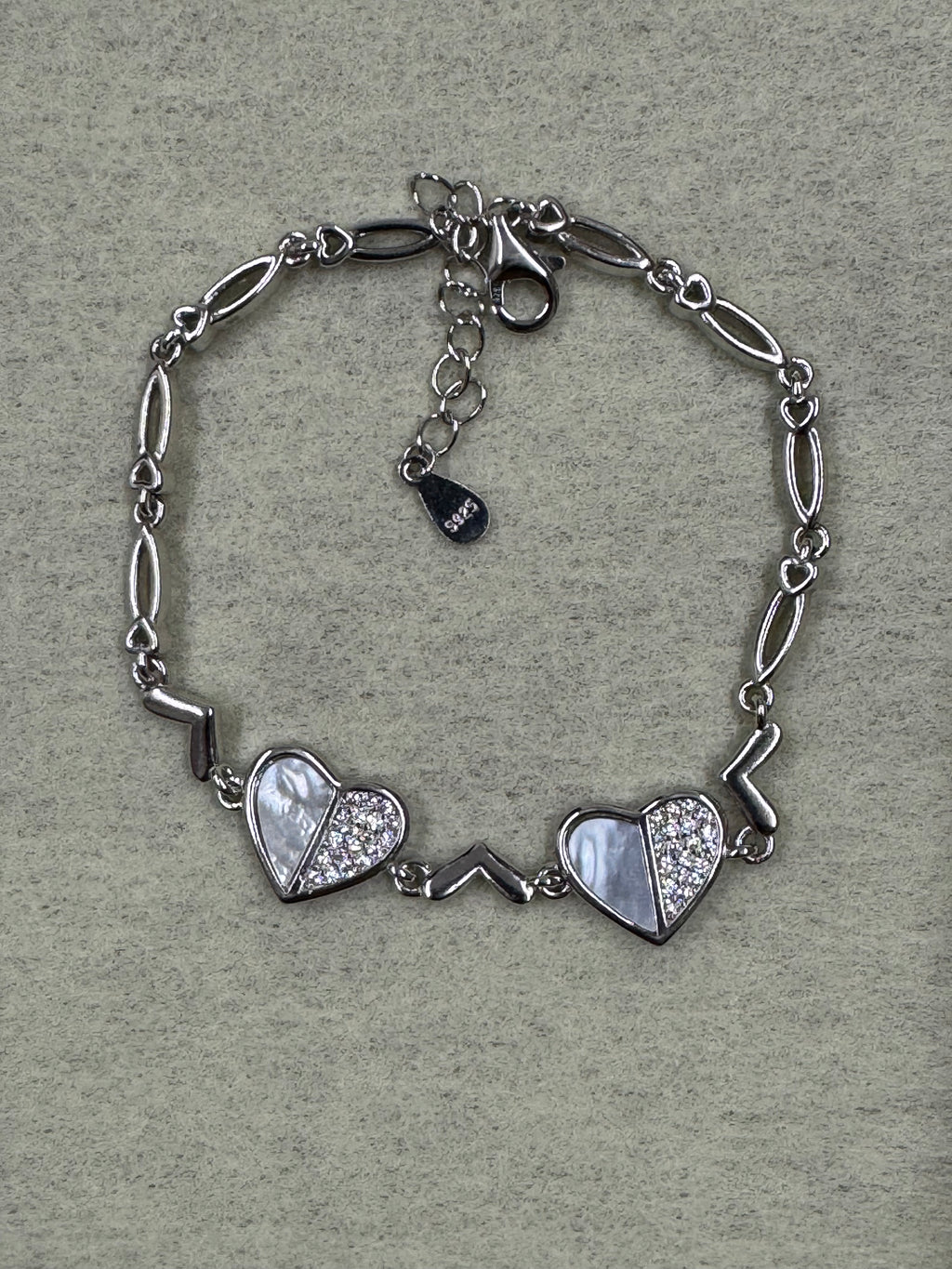 Flat lay of the sterling silver bracelet on grey felt, showing both cubic zirconia heart stations and the 925 tag on the extender.