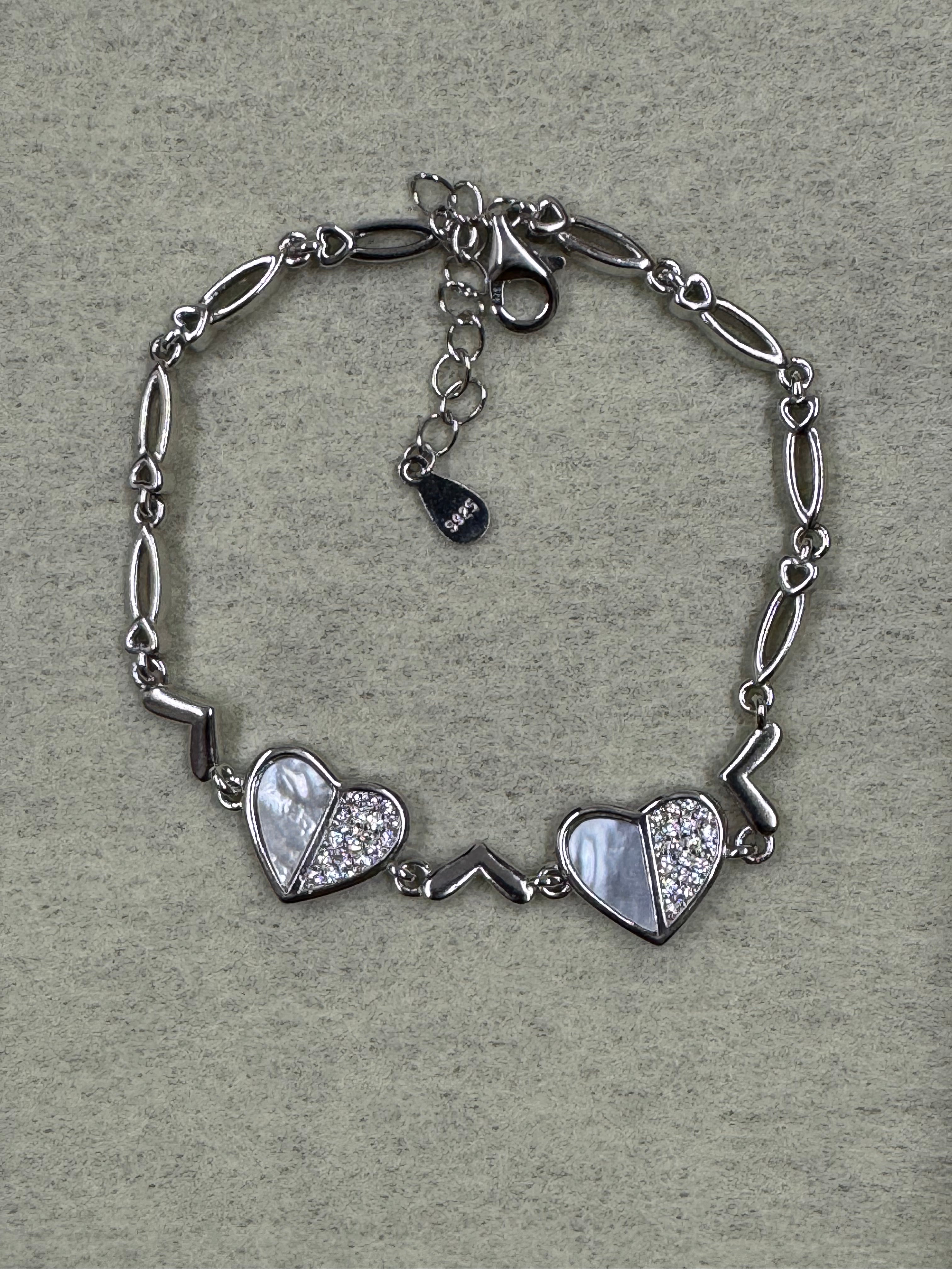 Flat lay of the sterling silver bracelet on grey felt, showing both cubic zirconia heart stations and the 925 tag on the extender.