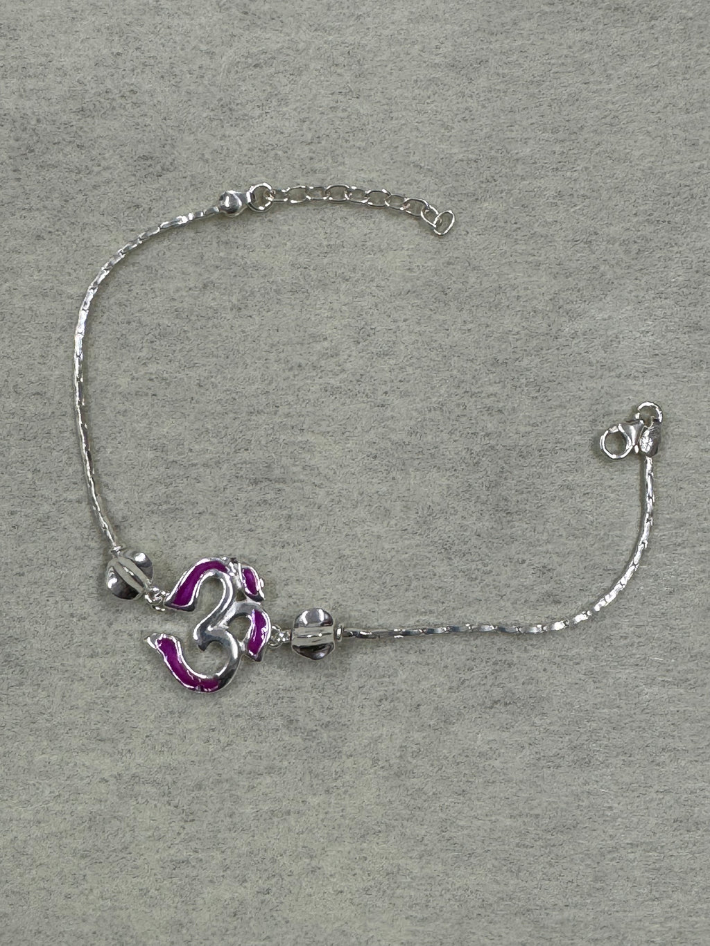 Sterling silver bracelet with a magenta enamel Om station on a fine flat chain, laid flat on grey felt.