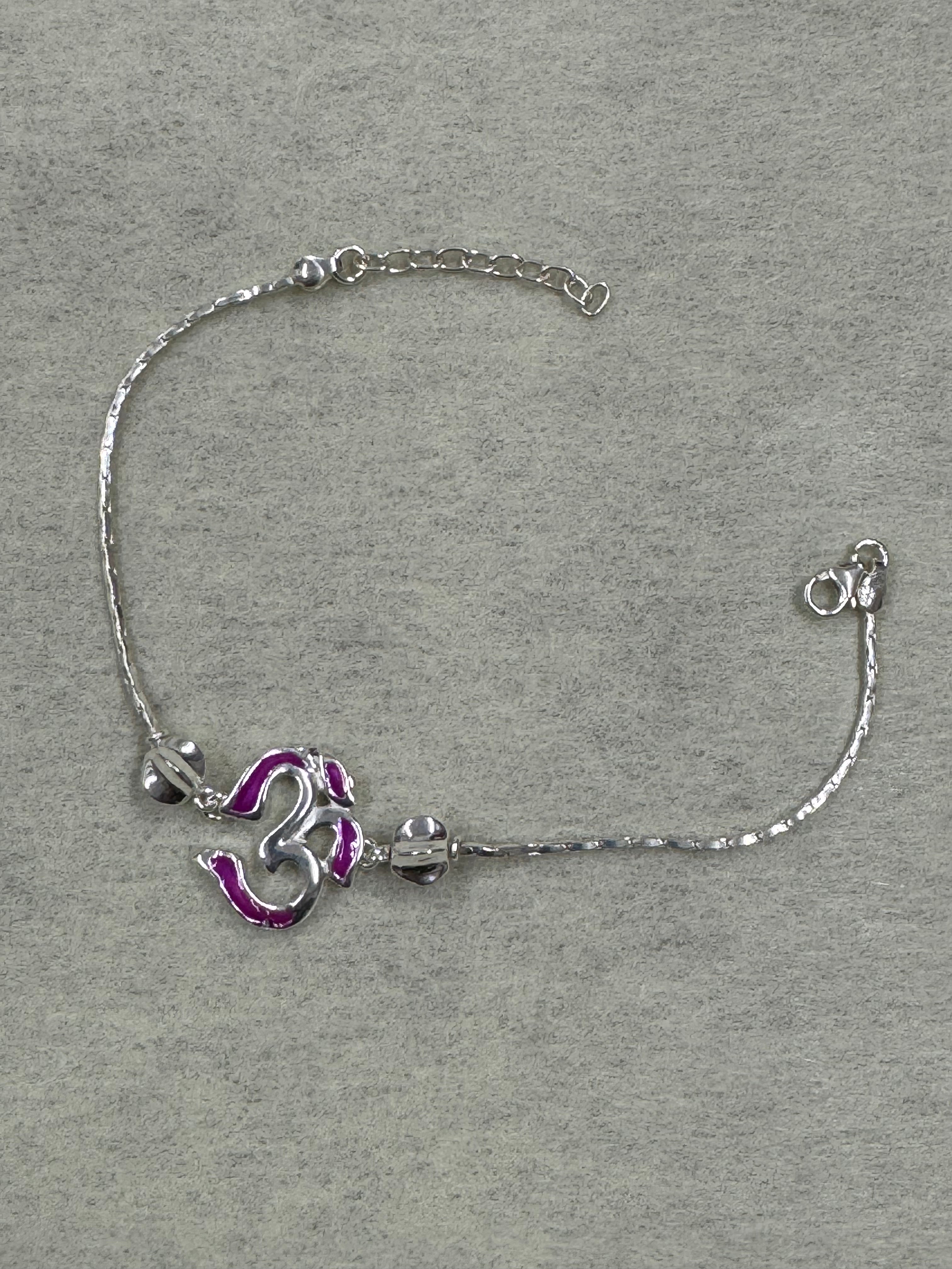 Sterling silver bracelet with a magenta enamel Om station on a fine flat chain, laid flat on grey felt.