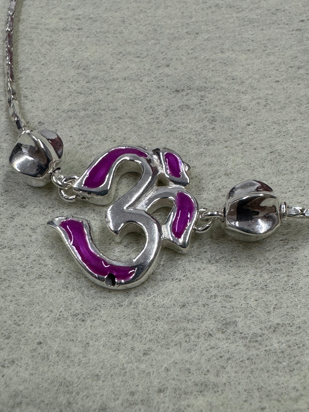 Close view of the magenta enamel Om station and the polished silver bead above it on the sterling silver bracelet.