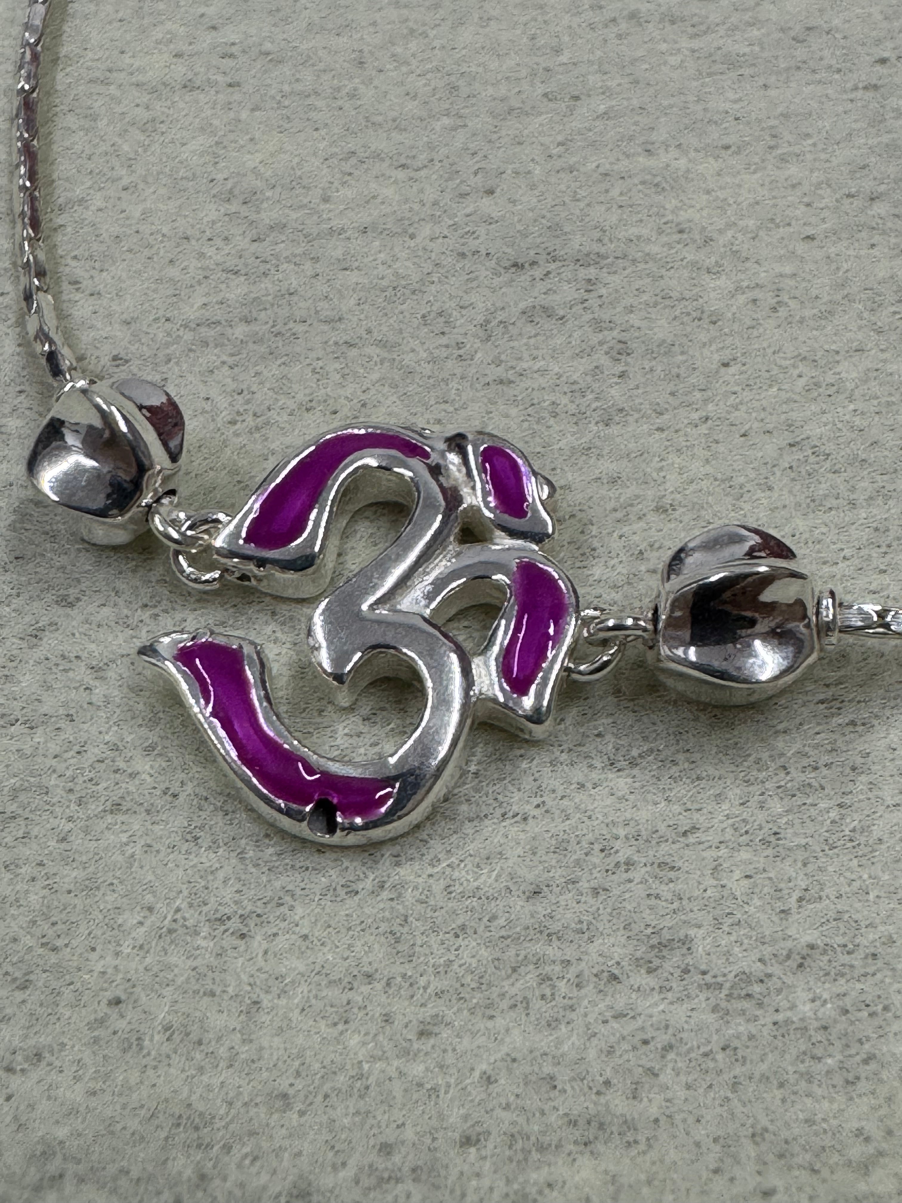 Close view of the magenta enamel Om station and the polished silver bead above it on the sterling silver bracelet.
