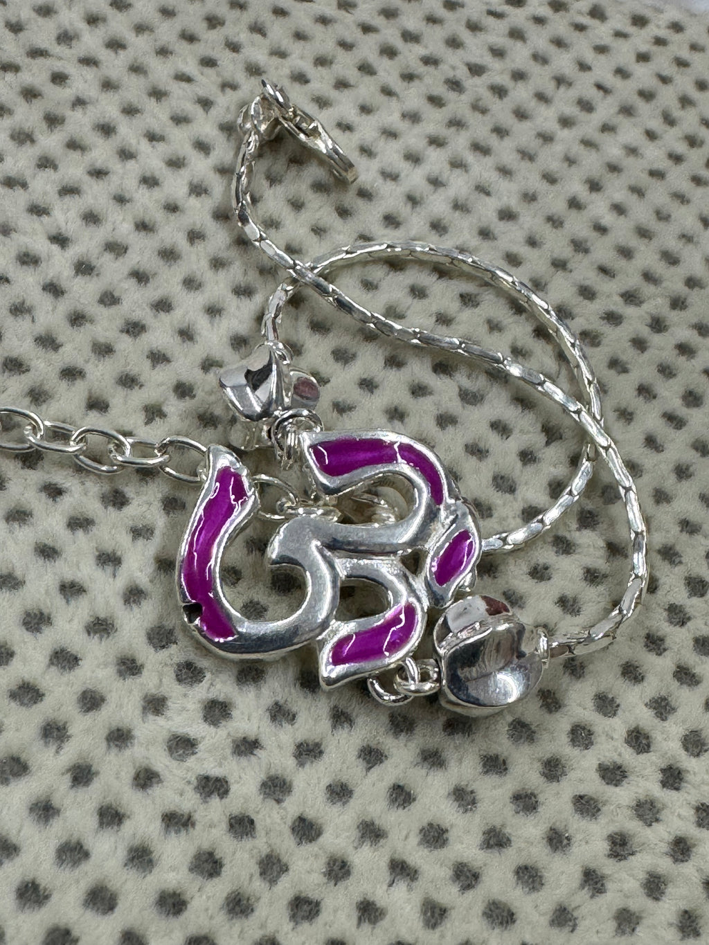 The enamelled Om station of the sterling silver bracelet, coiled on cream fabric with a dotted weave.