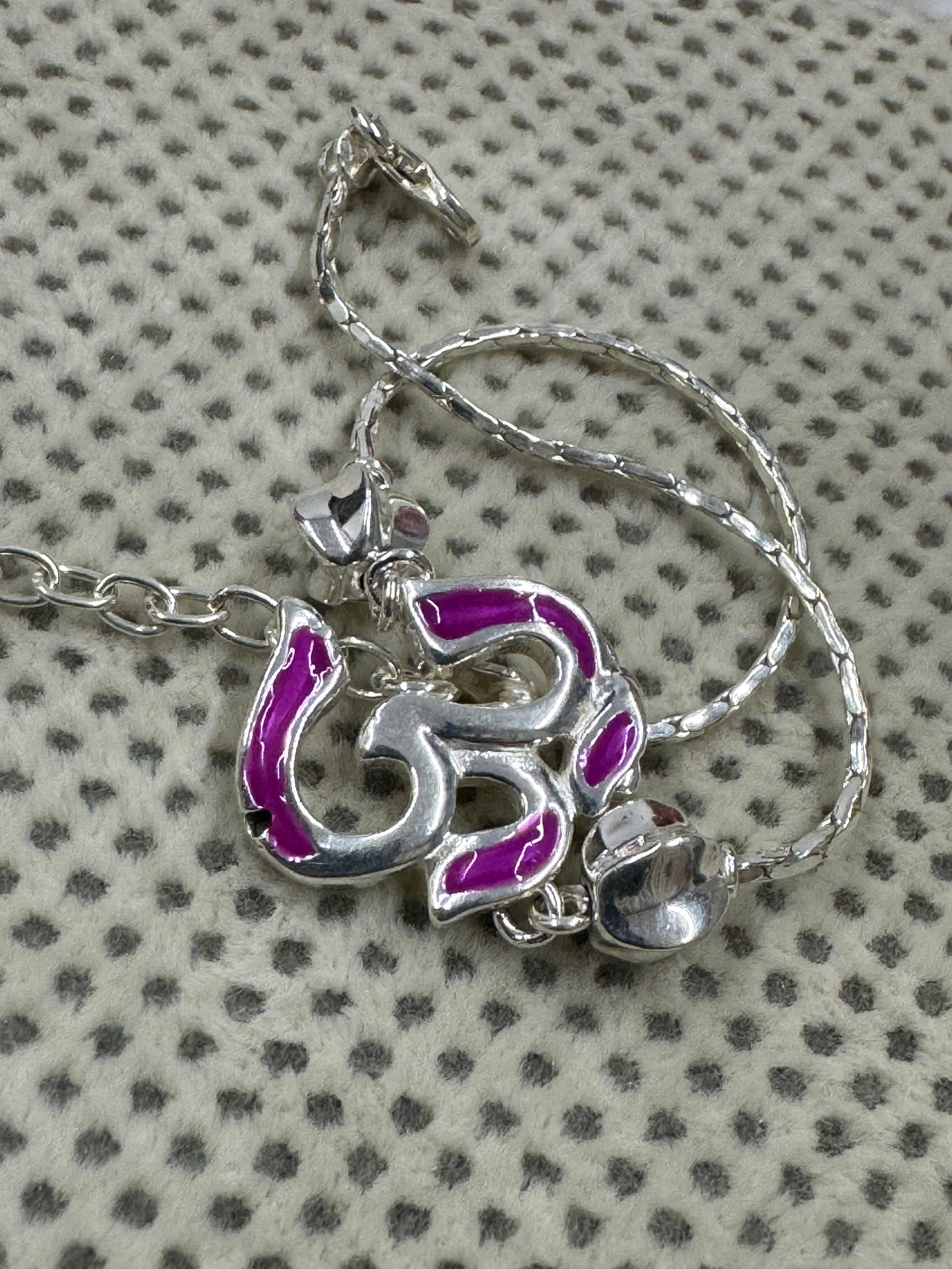 The enamelled Om station of the sterling silver bracelet, coiled on cream fabric with a dotted weave.