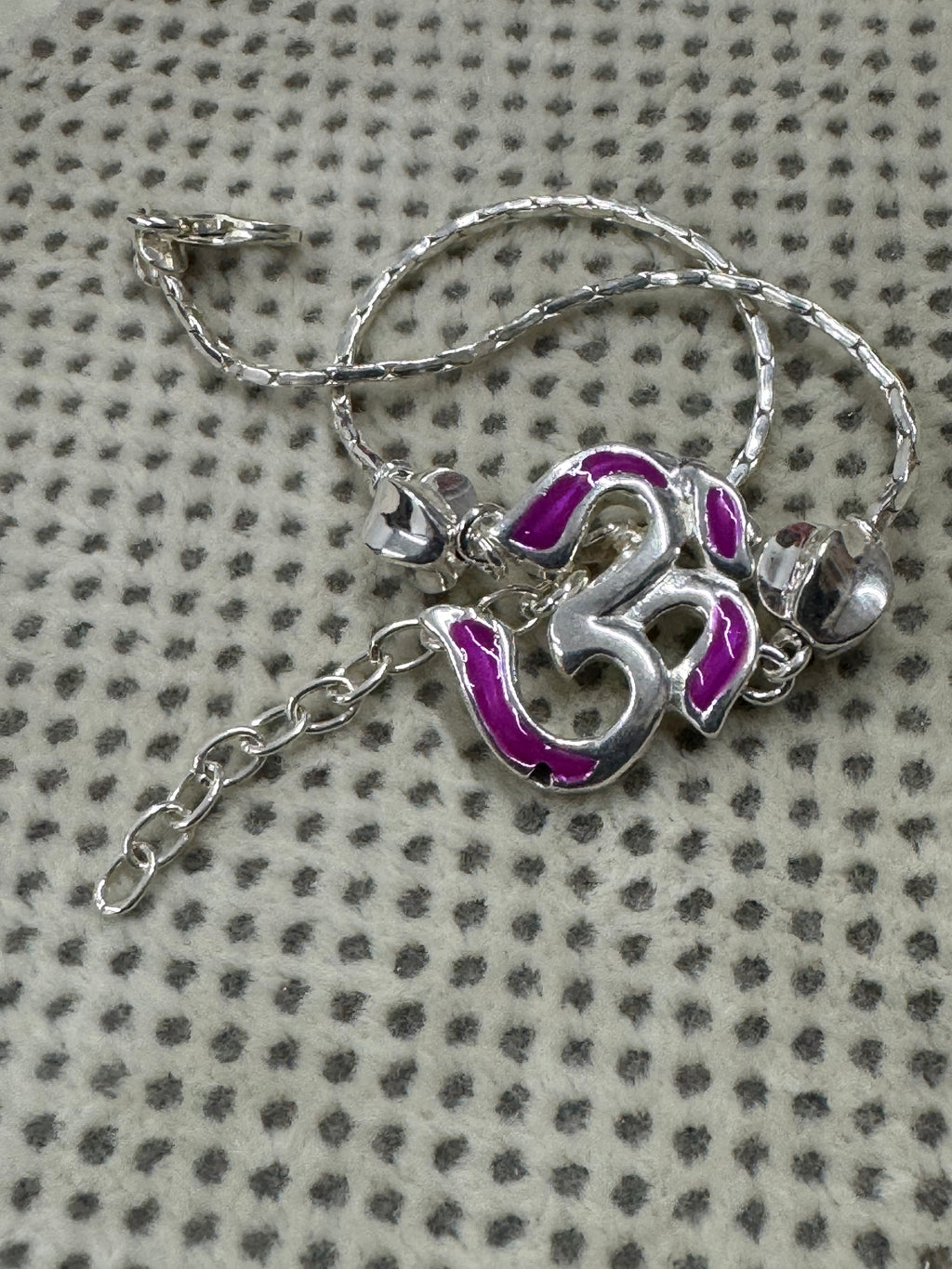 The sterling silver Om bracelet gathered on dotted cream fabric, with the extender chain trailing below.