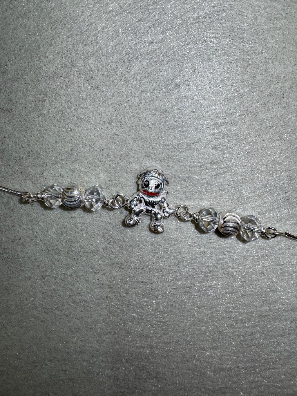 Sterling silver charm bracelet with a cast enamelled figure and faceted bead stations, laid on pale grey felt.