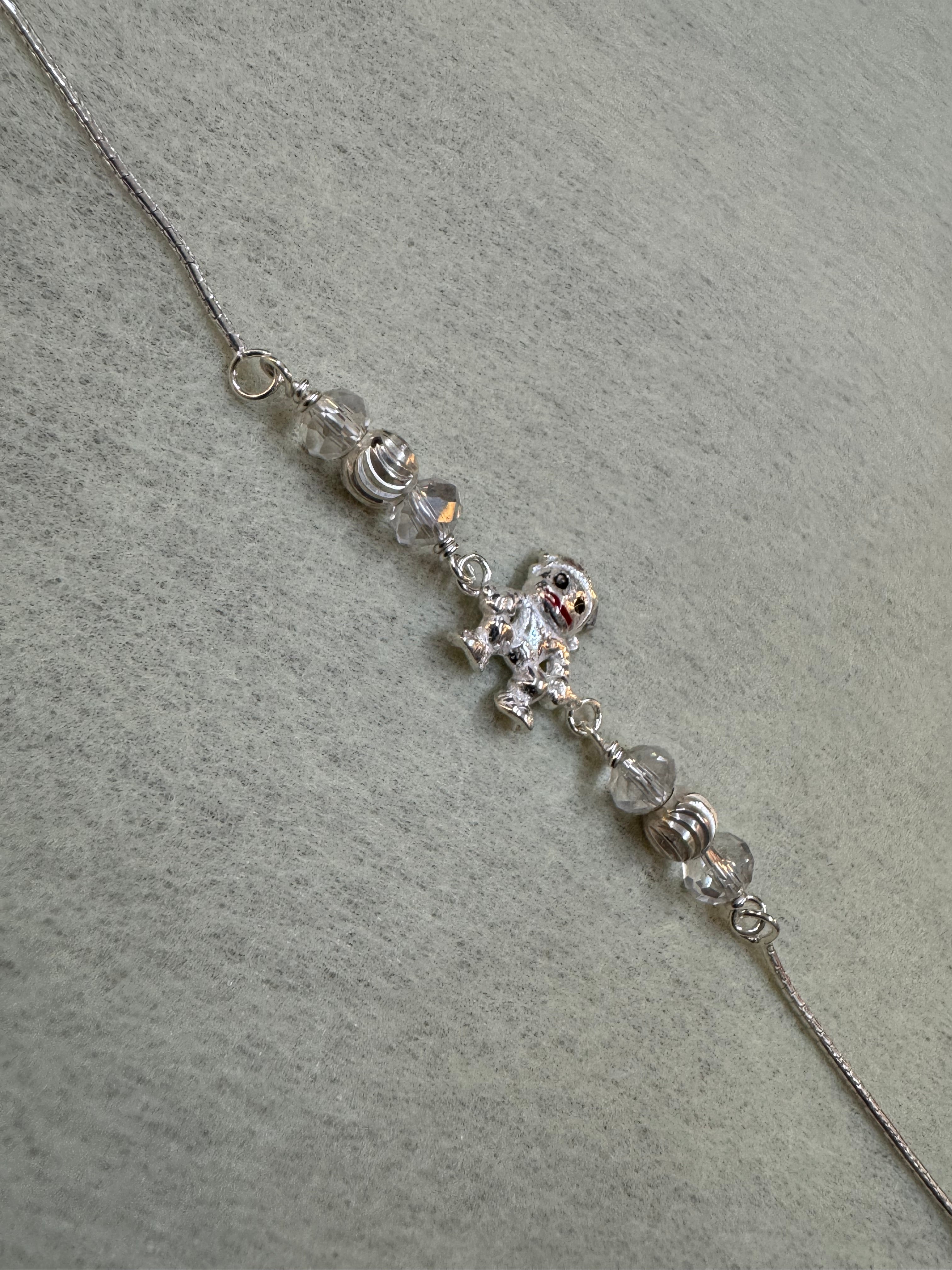 The sterling silver bracelet laid out straight, showing the central figure charm between two bead stations on a fine flat chain.