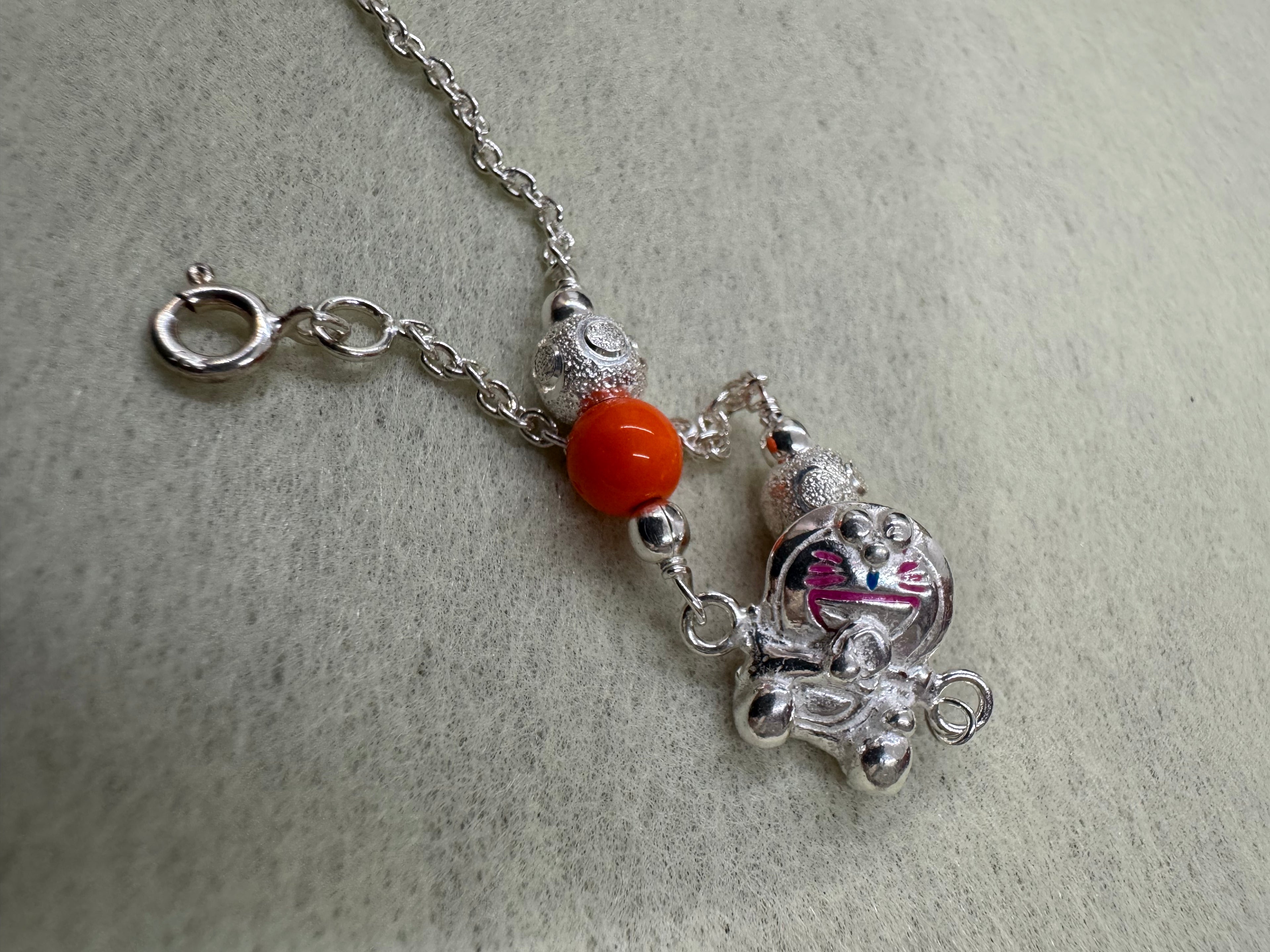 The cat station and one orange bead on a fine sterling silver chain, with the spring ring clasp open to the right.