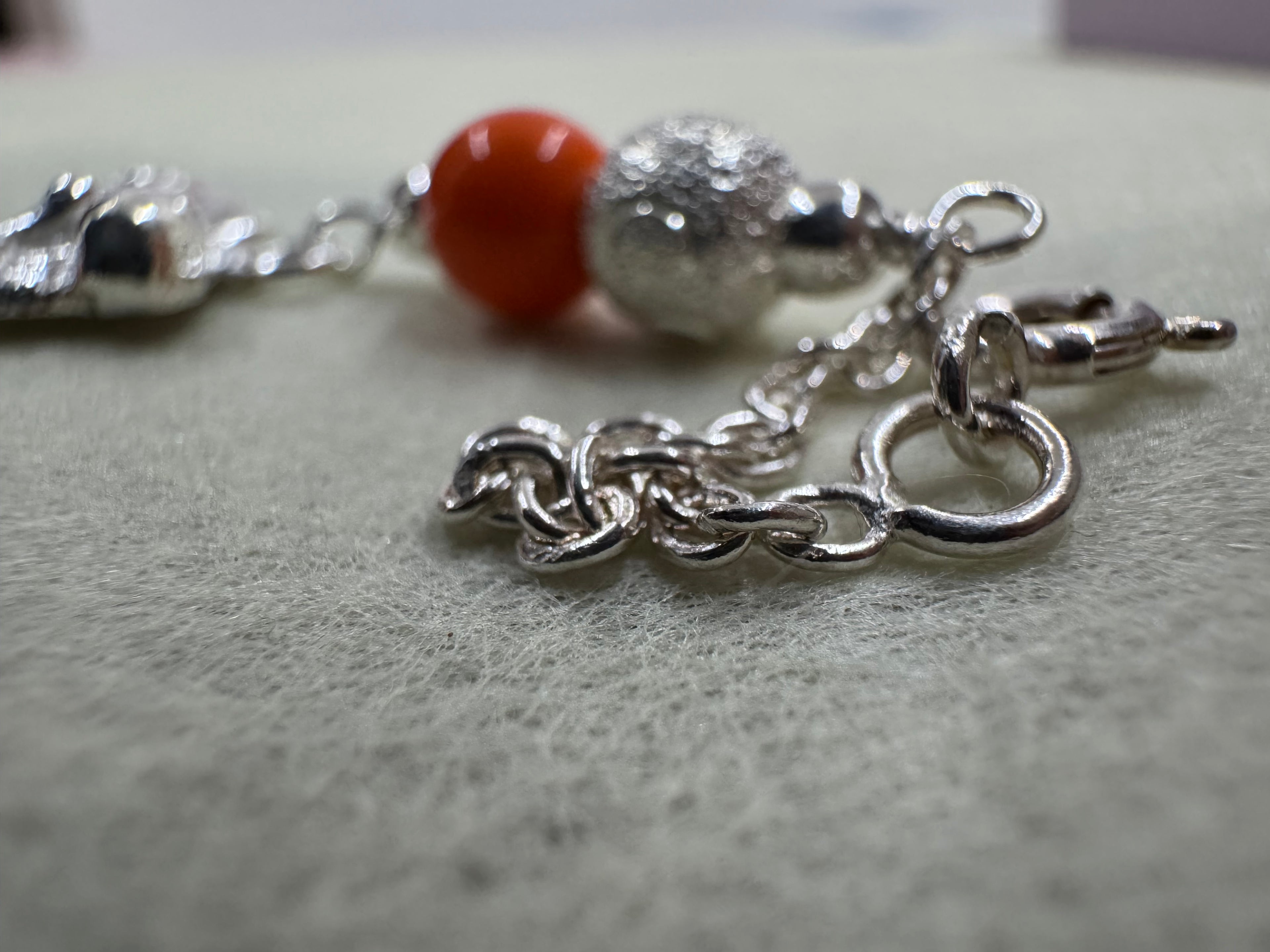 Close view of the extender chain and spring ring on the sterling silver cat bracelet, with an orange bead behind.