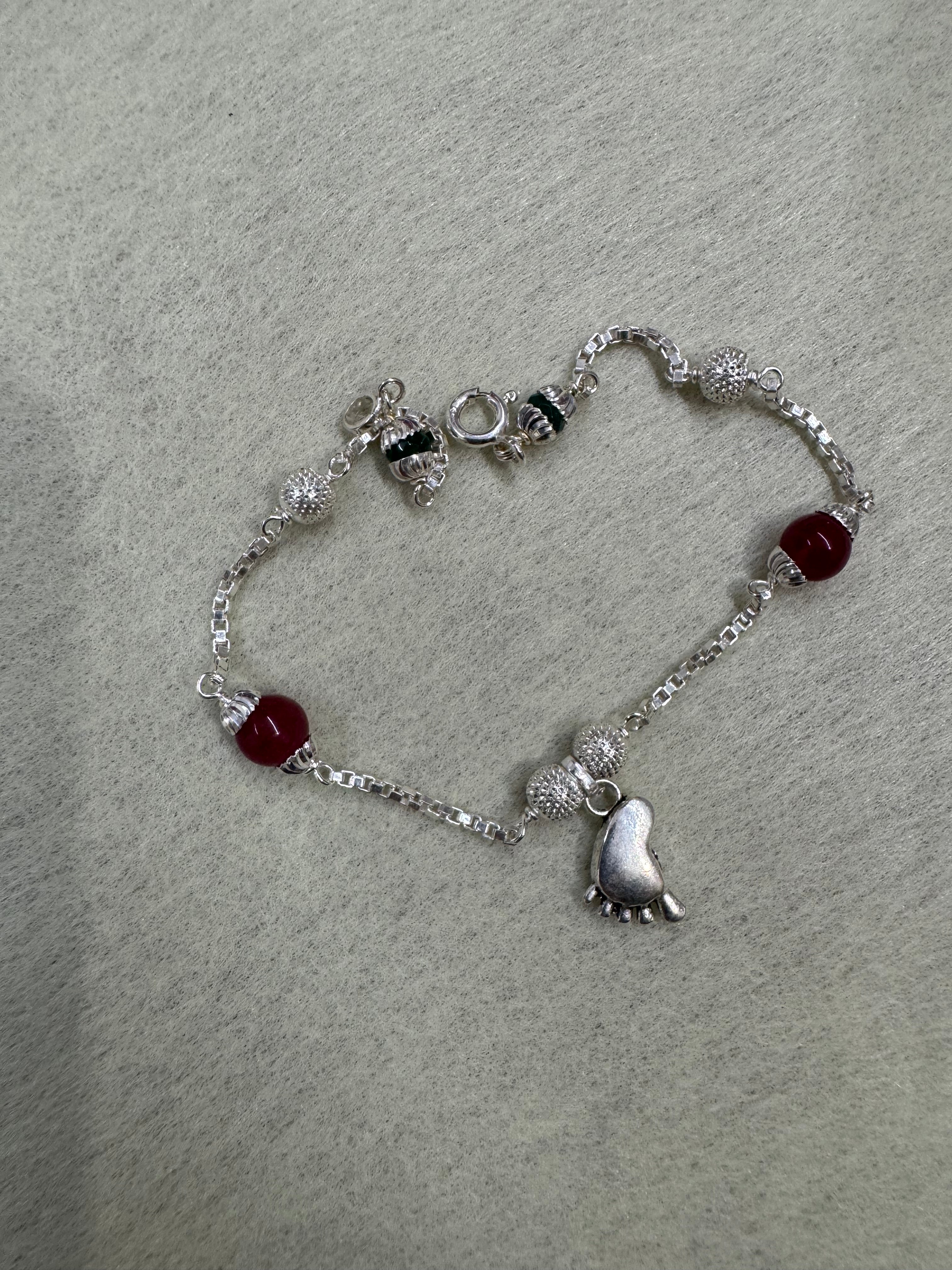 The sterling silver baby foot bracelet opened into a loop on grey felt, showing the spring ring clasp and the spacing of the stations.