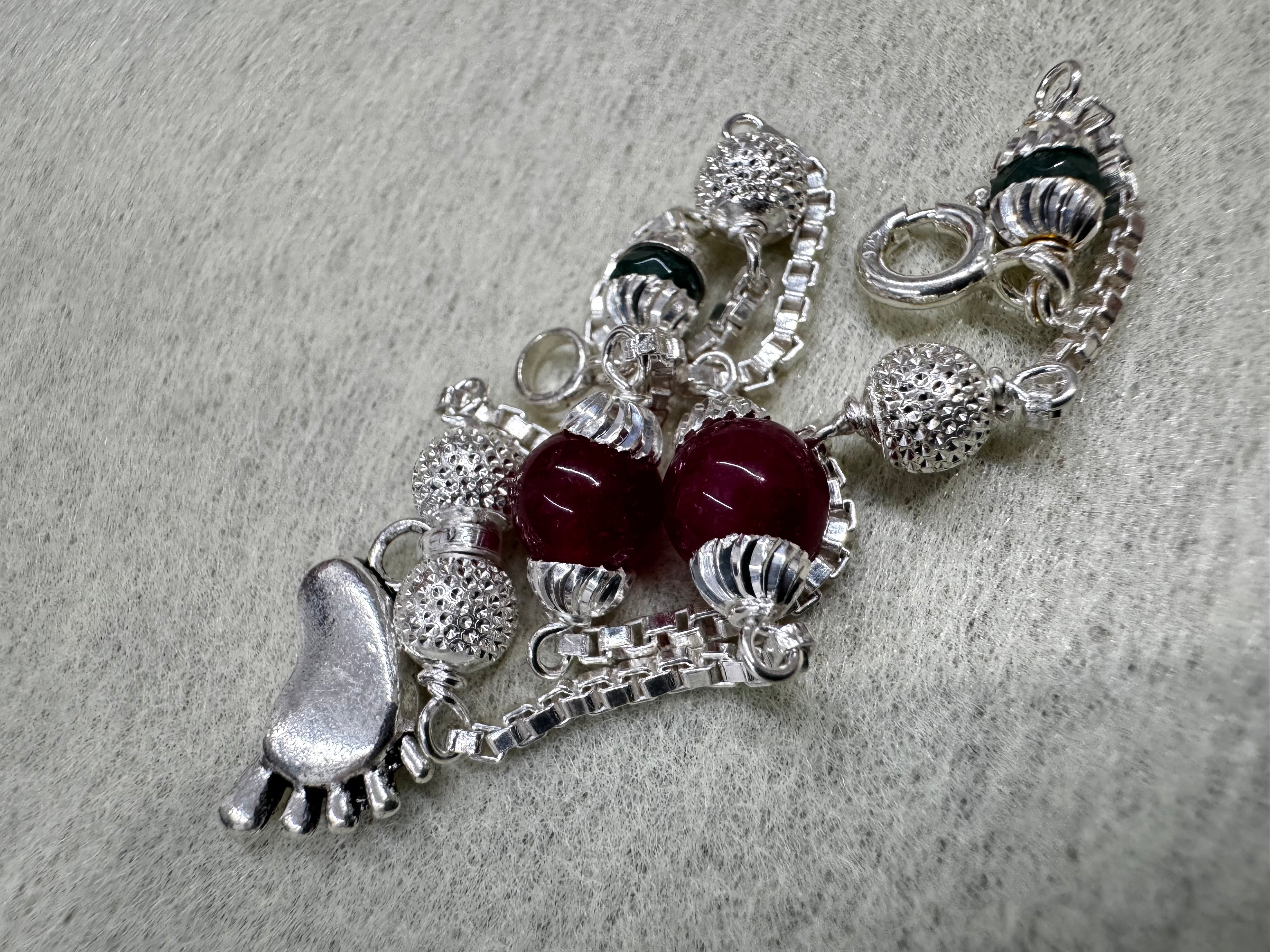 Close view of the cast baby foot charm and the fluted caps on the red beads of the sterling silver bracelet.