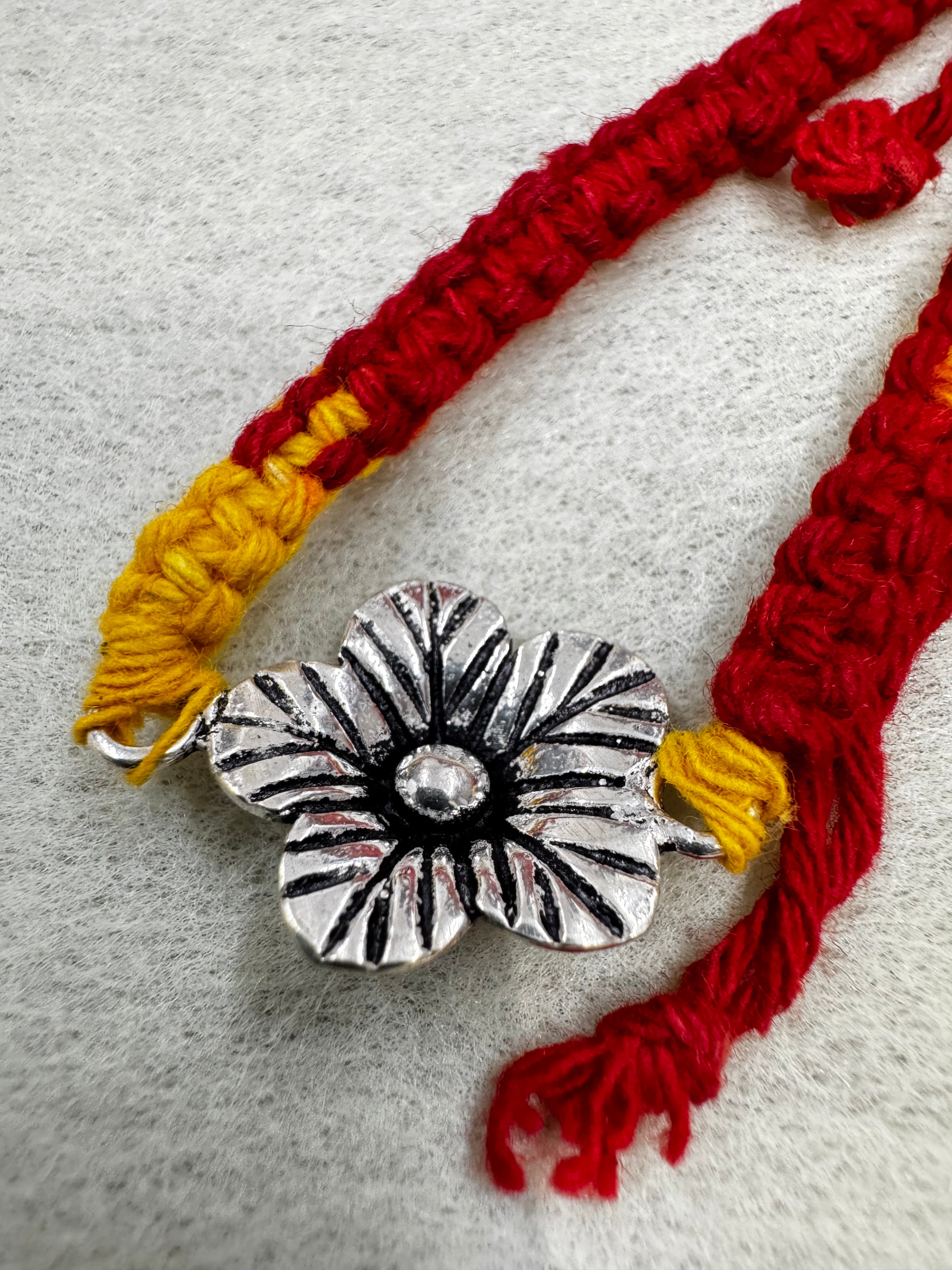 Cast sterling silver flower with oxidised line-work on a woven red and yellow cotton thread bracelet.