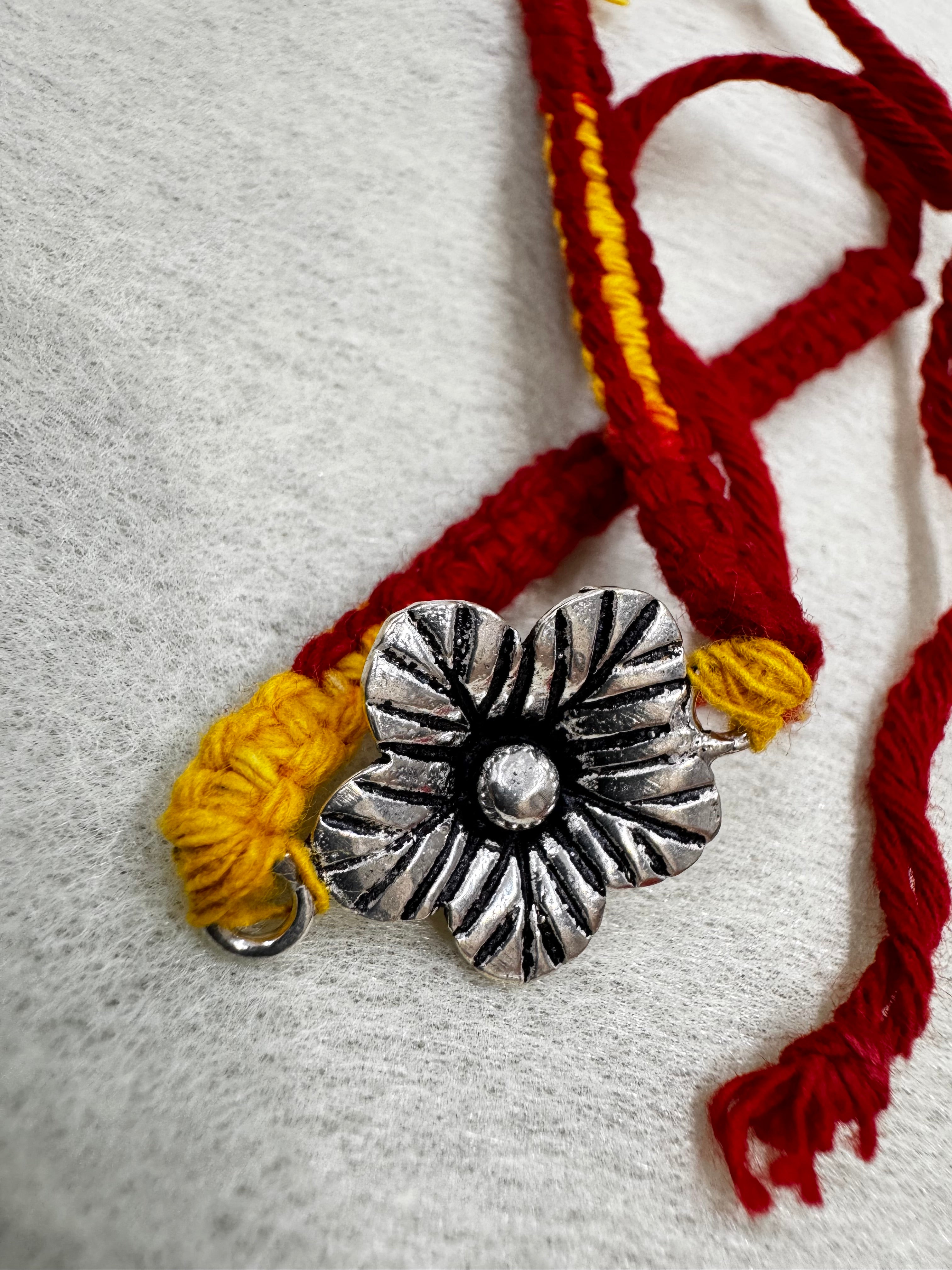The sterling silver flower and the woven red thread band, with the loose ties folded behind on white felt.