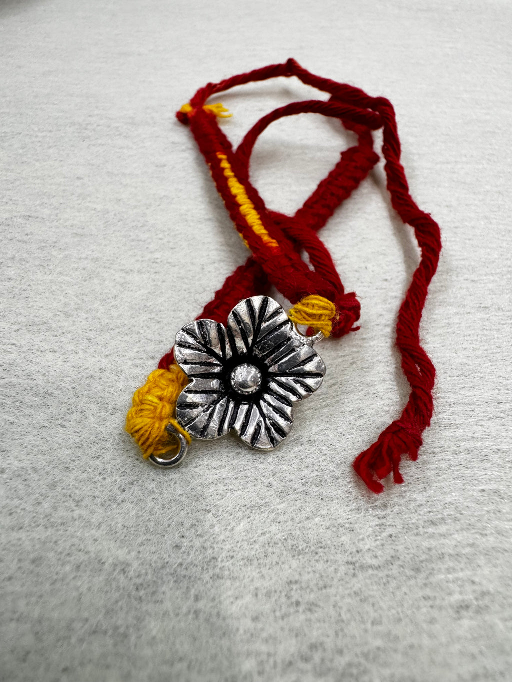 The sterling silver flower bracelet coiled on white felt, with the cotton ties looped to the left.