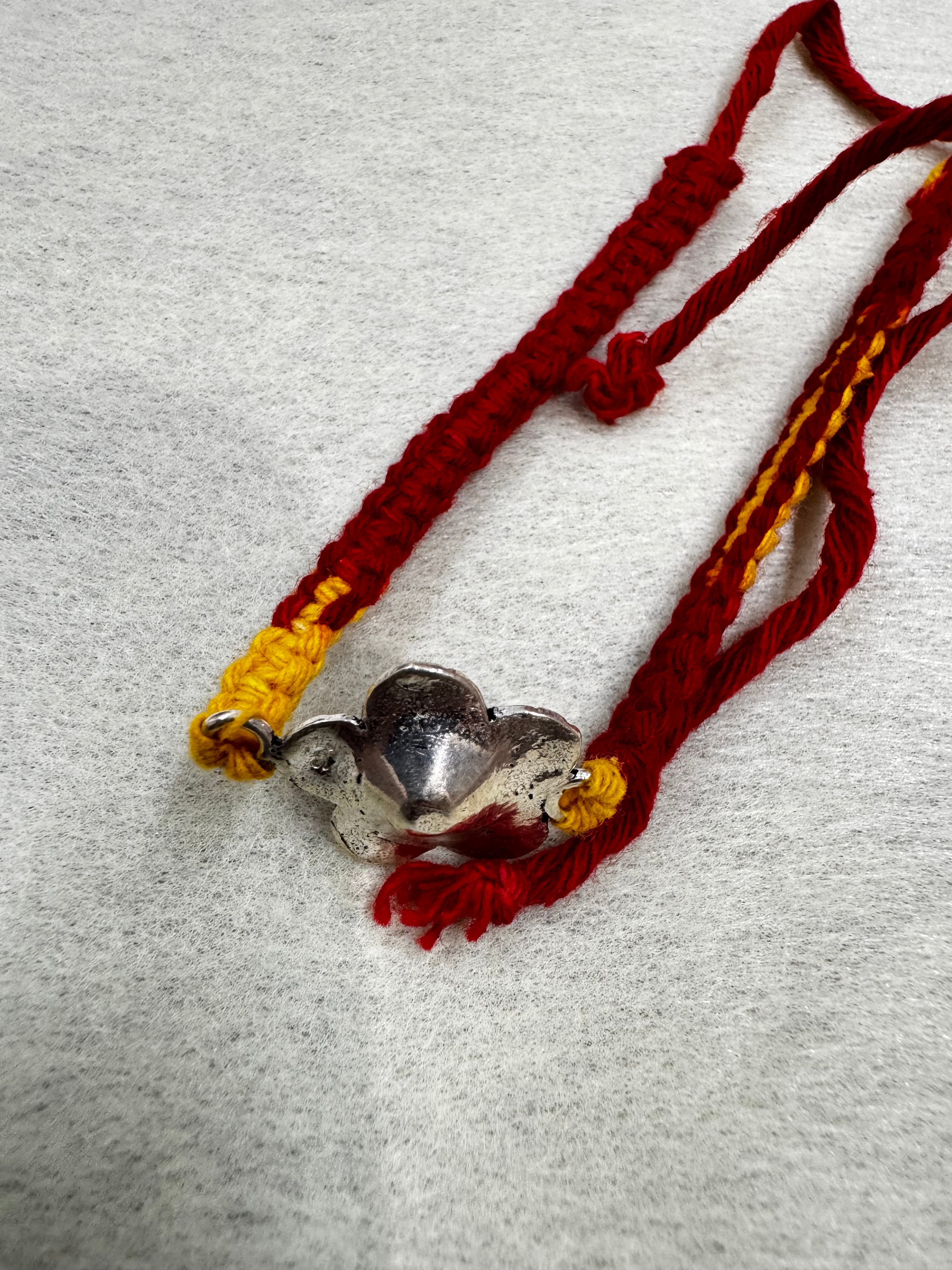 Reverse of the sterling silver flower on the woven thread bracelet, showing the plain domed back.