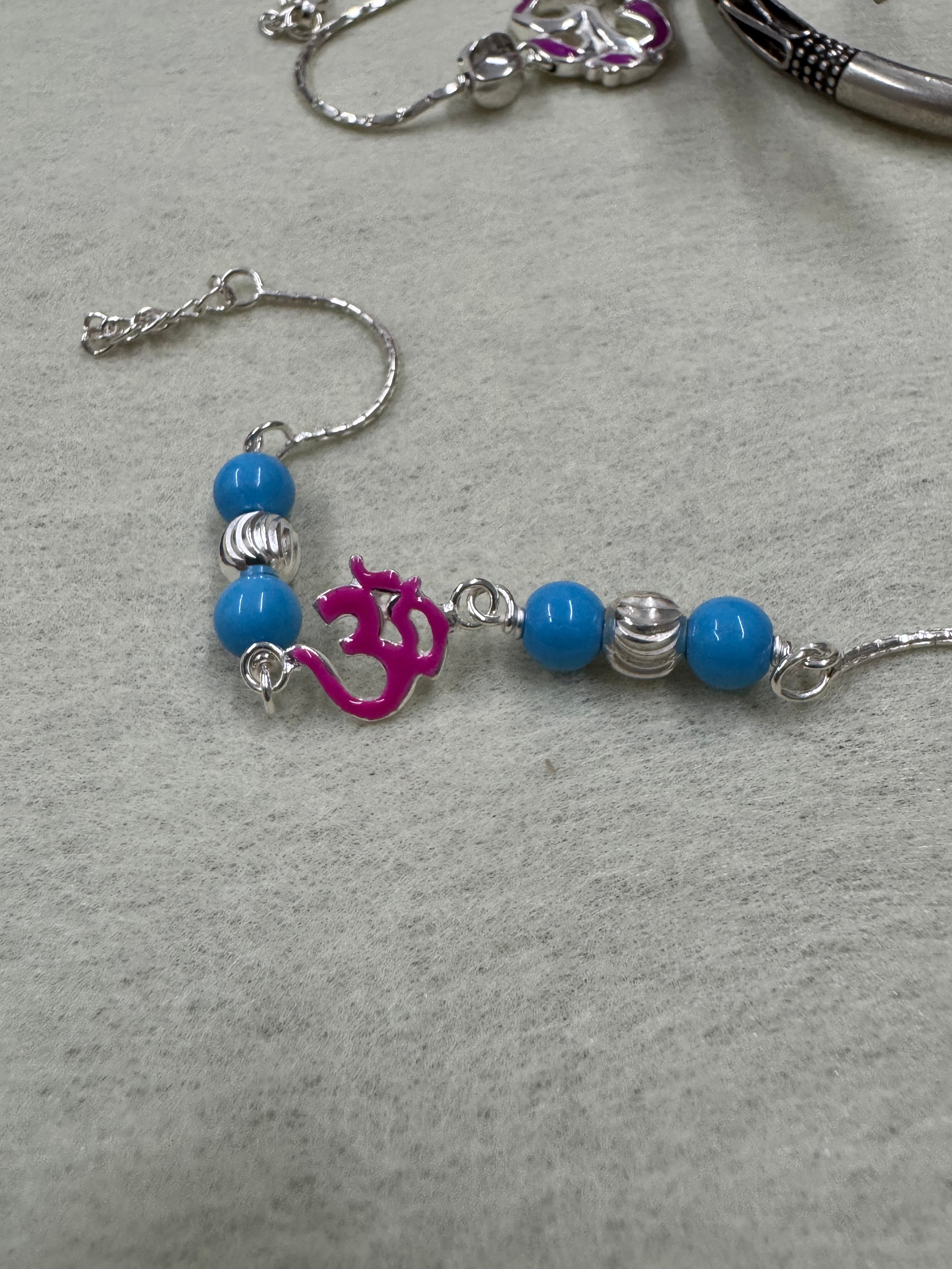 Sterling silver beaded bracelet with blue beads, fluted silver rondelles and a magenta enamel Om motif, laid on grey felt.
