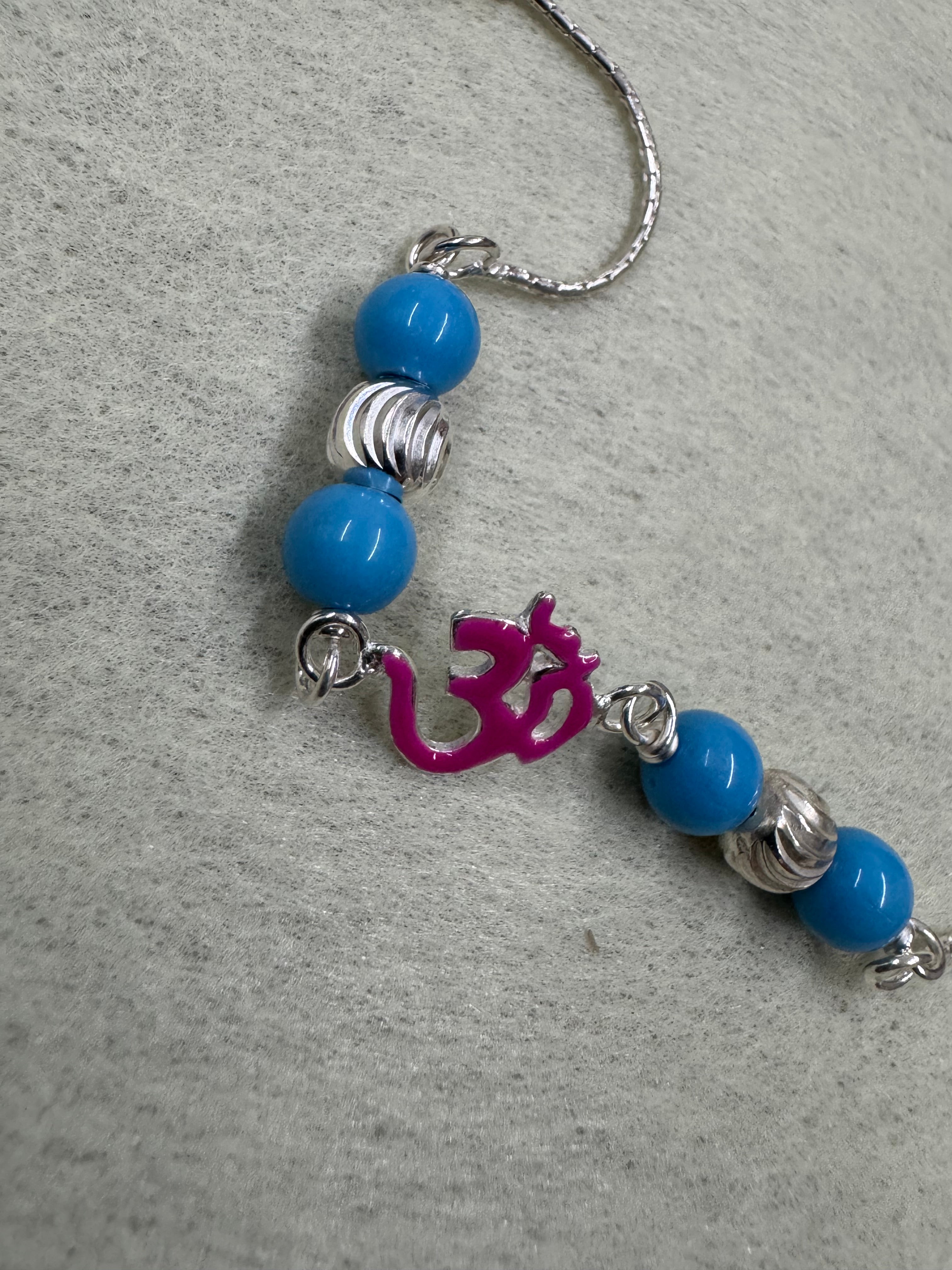 Close view of the beaded station on the sterling silver bracelet, showing the jump rings, fluted rondelles and the magenta enamel Om.