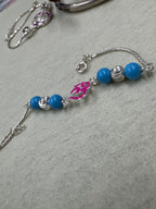 The full sterling silver beaded bracelet curved on grey felt, showing four blue beads, two fluted rondelles and the enamel Om at the centre.